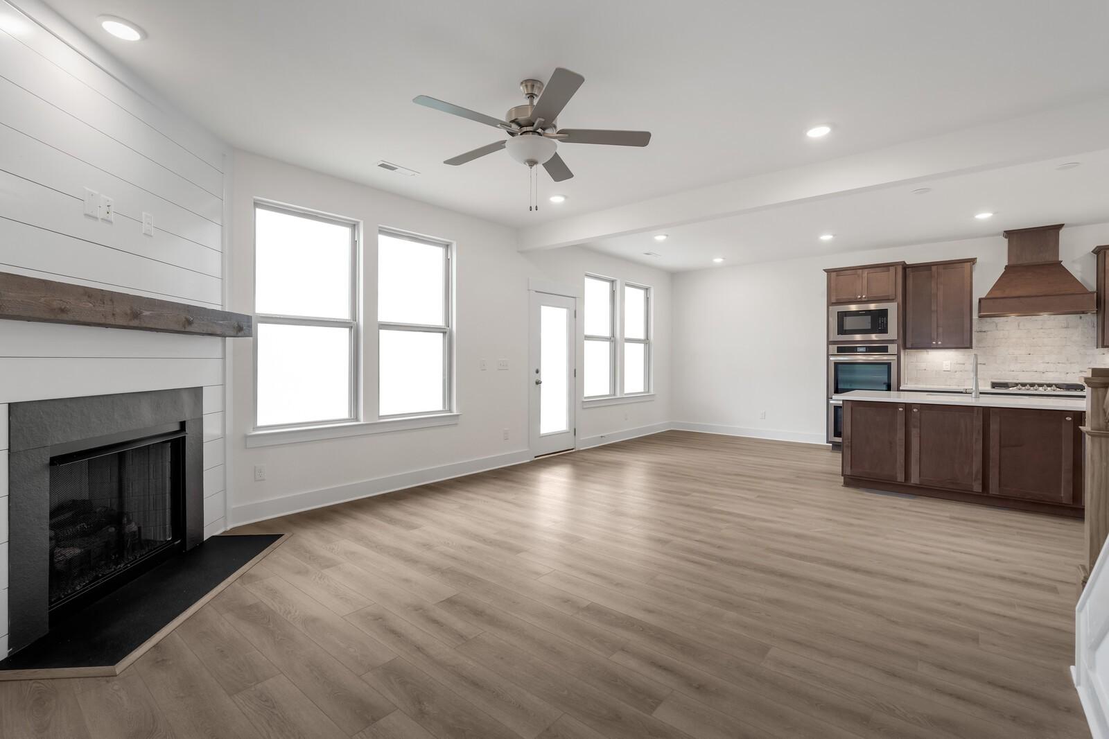Open-concept great room with shiplap fireplace, ceiling fan, and adjacent kitchen with shaker cabinets in Davidson Homes The Willow C, Gallatin, TN