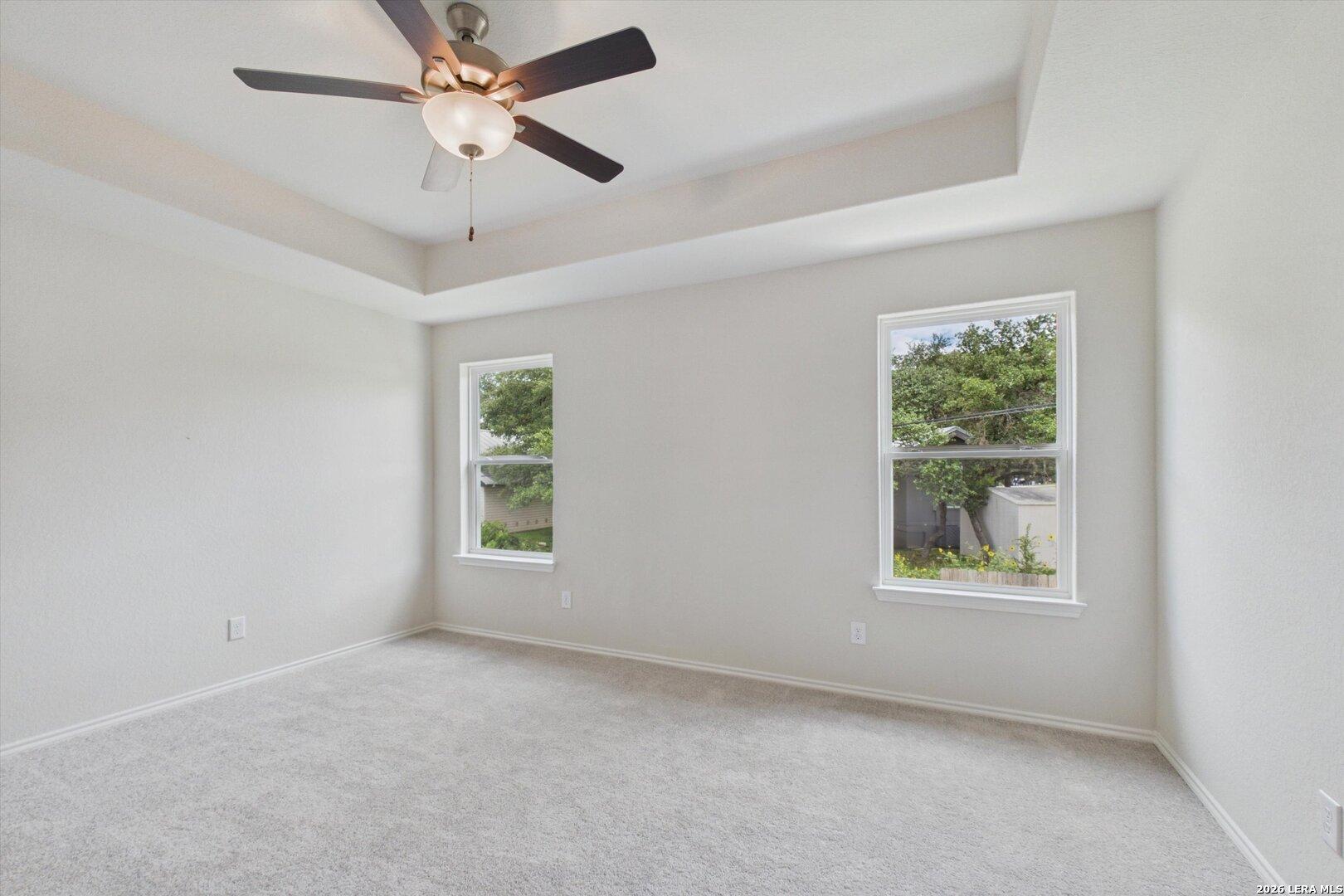 Bright bedroom with tray ceiling and ceiling fan in The Charlotte B floor plan at Meadows at Oak Creek, San Antonio.