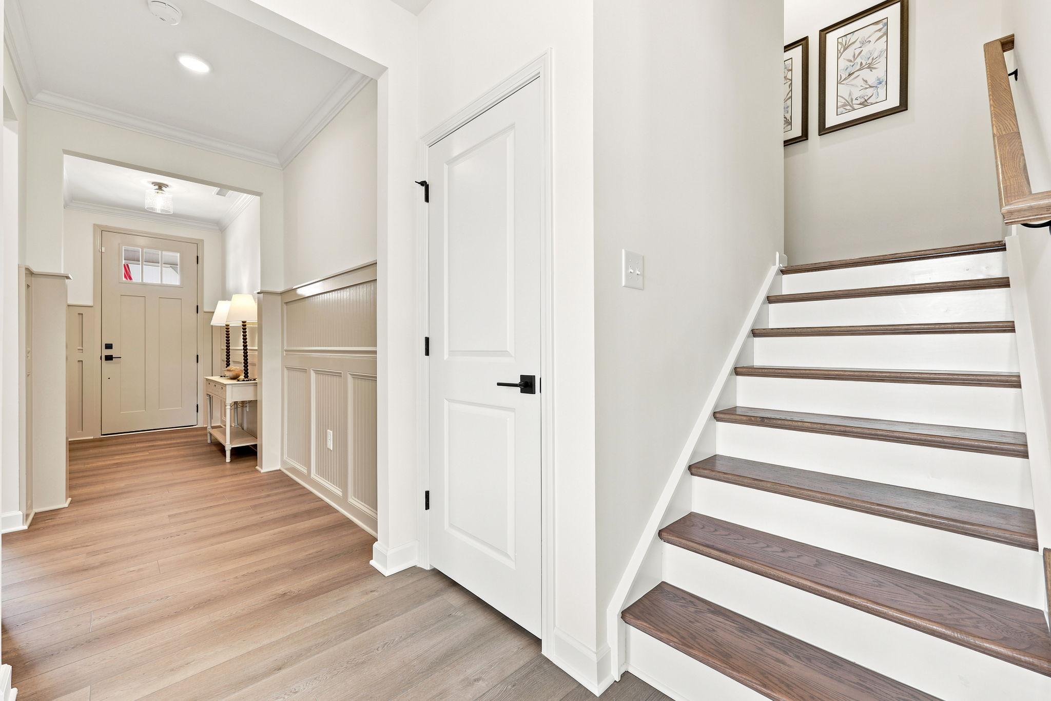 Foyer and staircase in The Beech B home design featuring white wainscoting, wood flooring, and elegant entryway.