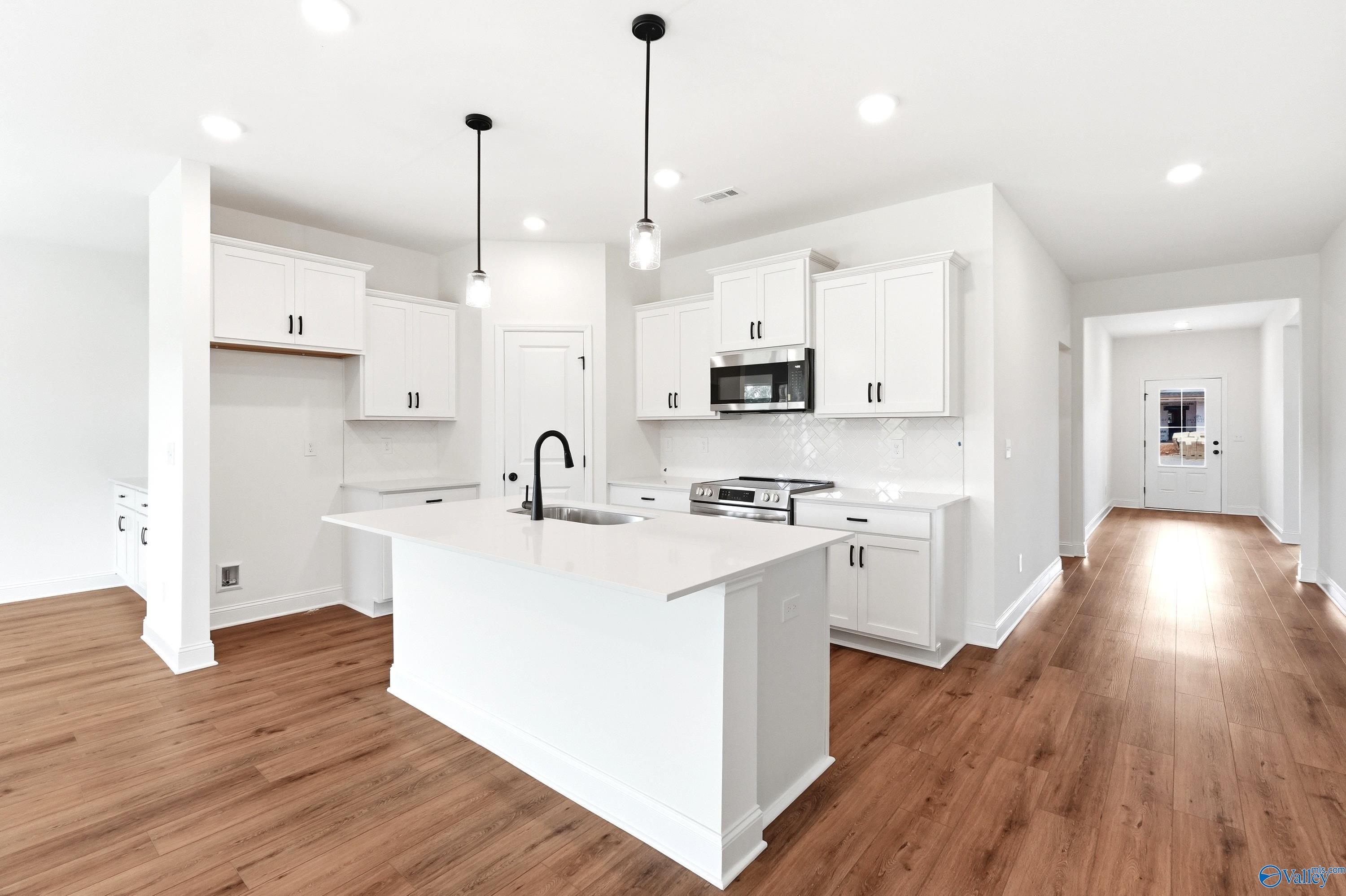 Modern kitchen with white cabinets, quartz island, and wood floors in The Daphne C floor plan by Davidson Homes in Toney.