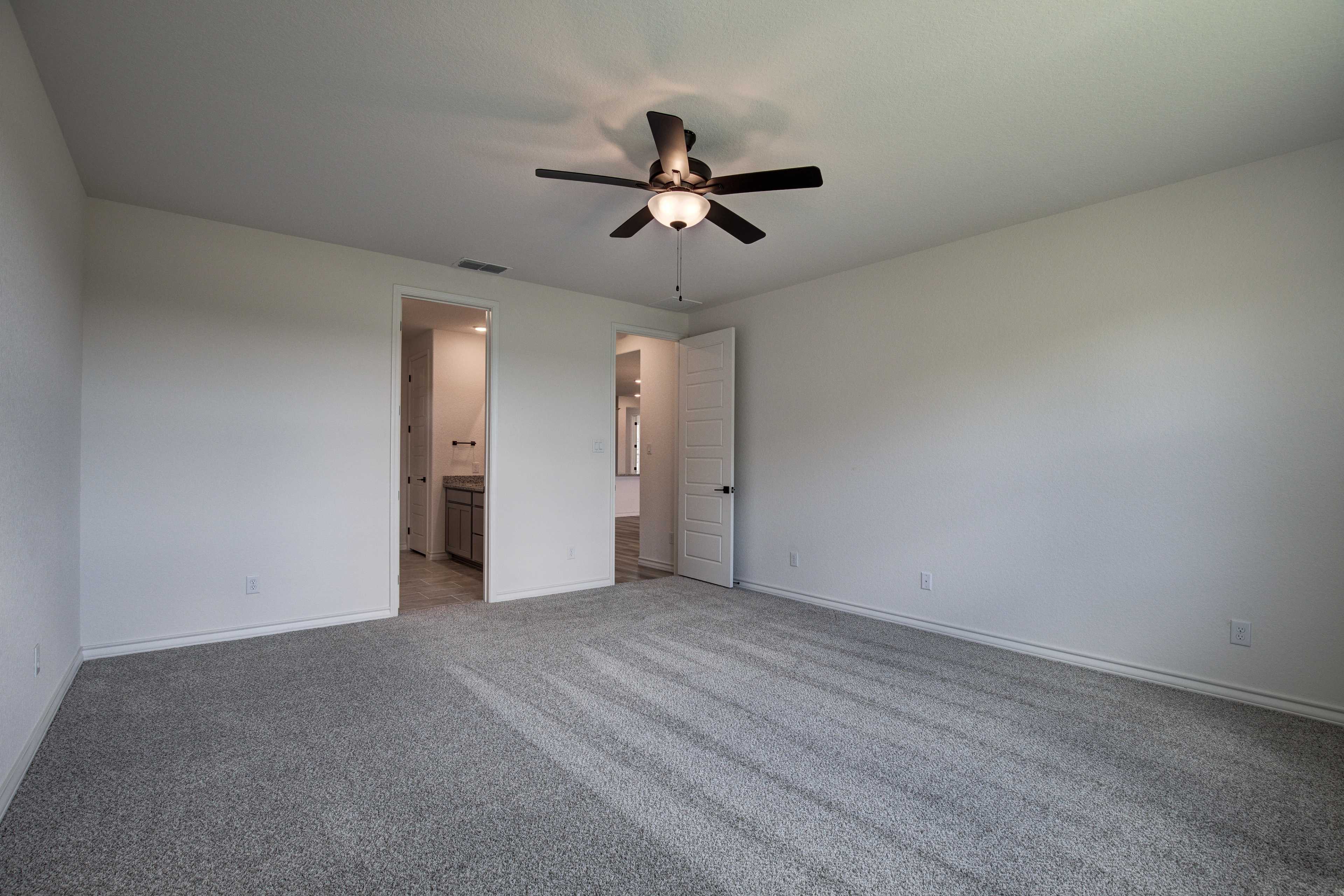 Spacious master bedroom in The Lanier with ceiling fan, en-suite bath access, gray carpet, and white walls