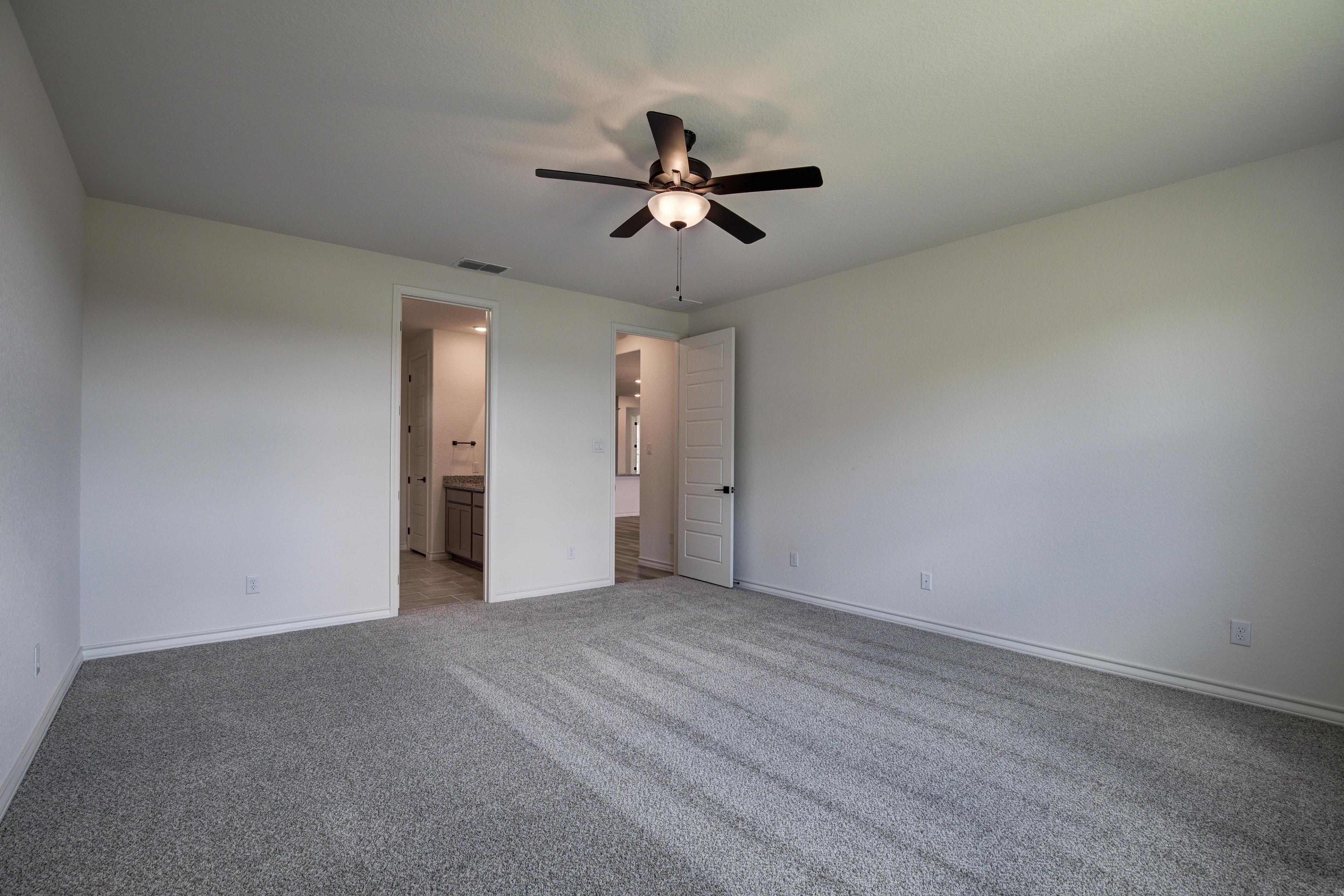 Spacious master bedroom in The Lanier F with gray carpet, ceiling fan, white walls, and ensuite bathroom doorway