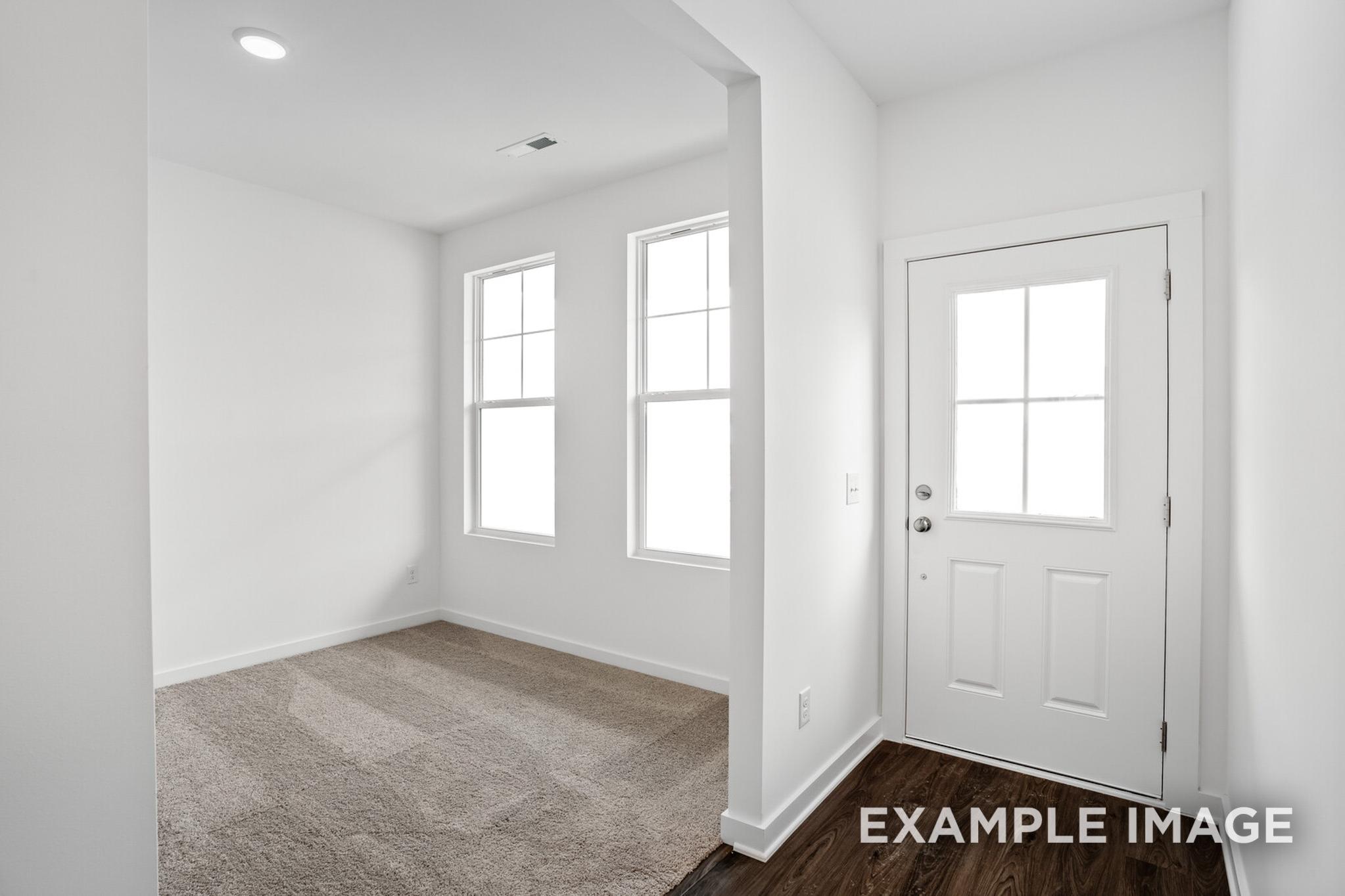 Spacious empty bedroom in The Logan C home with large double windows, white paneled door, and neutral carpet flooring