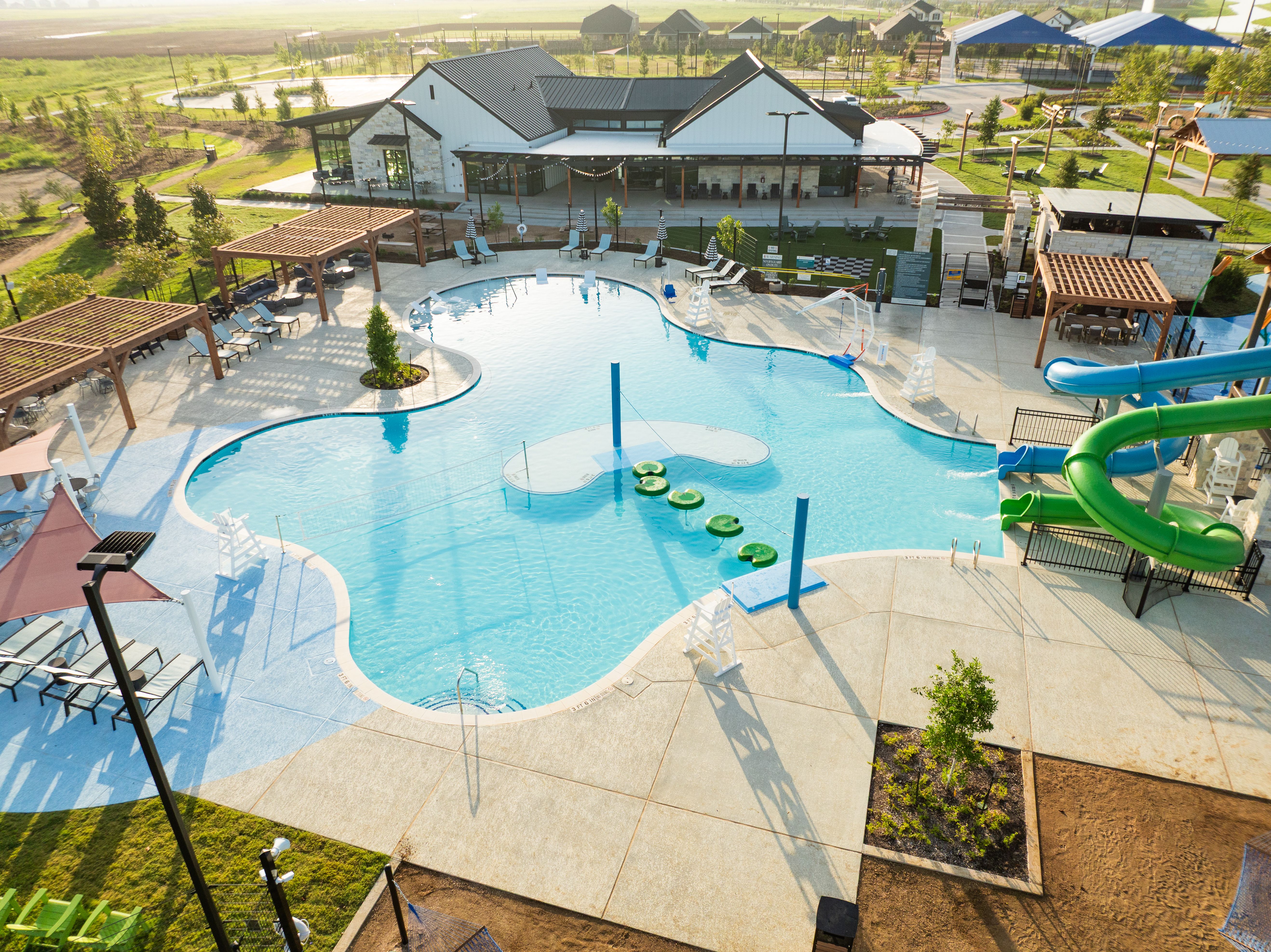 Resort-style swimming pool at Emberly in Beasley, Texas with green water slide, lily pads, cabanas and lounge seating