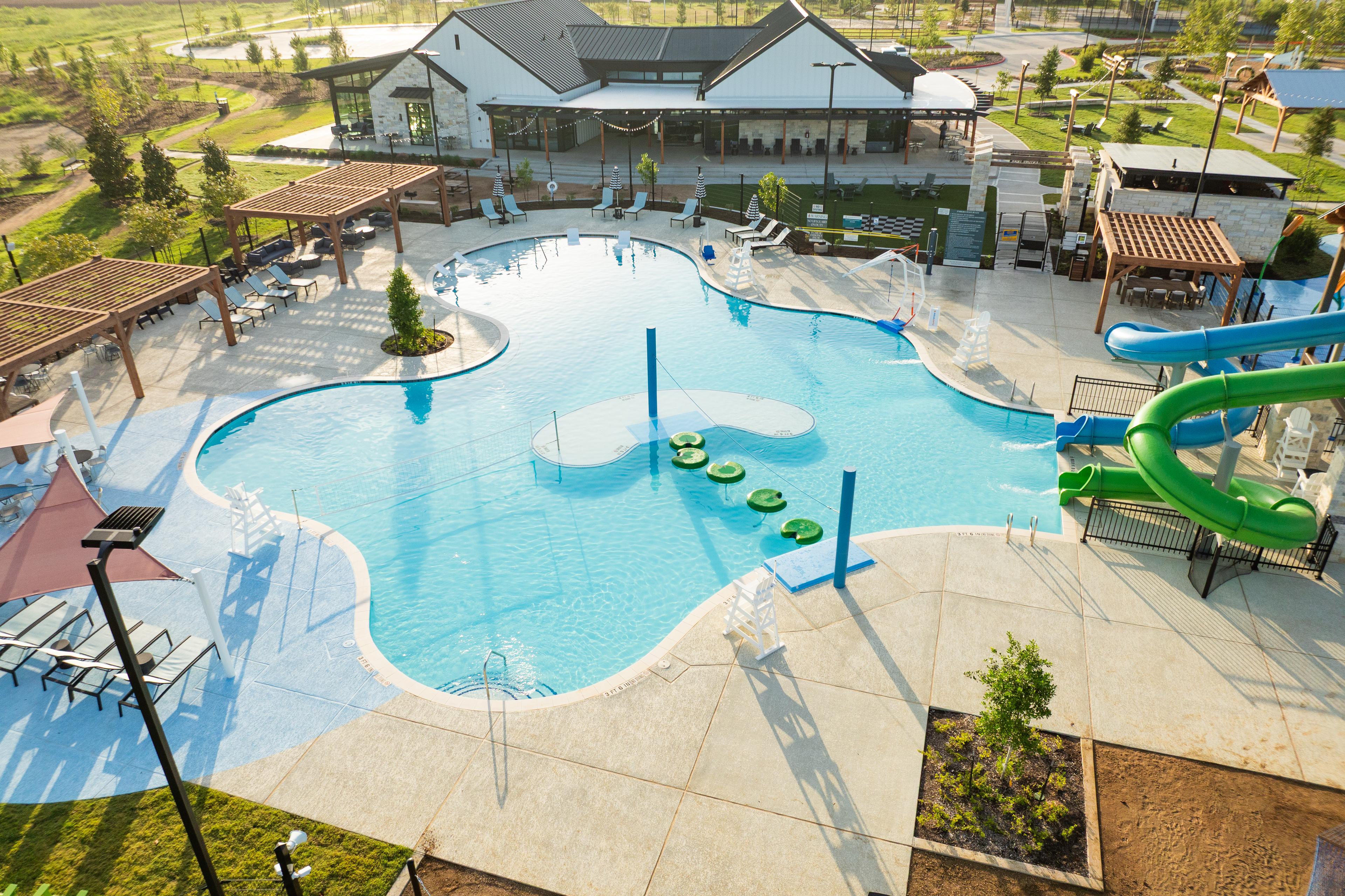 Resort-style swimming pool at Emberly in Beasley, Texas with green water slide, lily pads, cabanas and lounge seating
