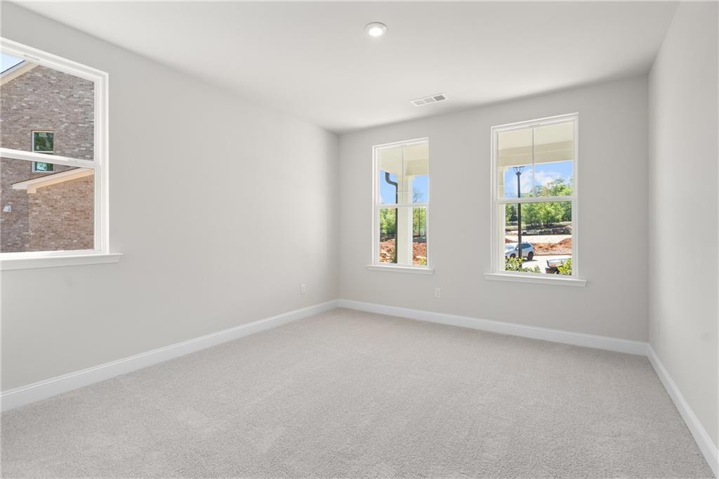Bright empty bedroom with light gray walls, beige carpet, and large windows overlooking greenery in The Hickory E home, Buford, GA