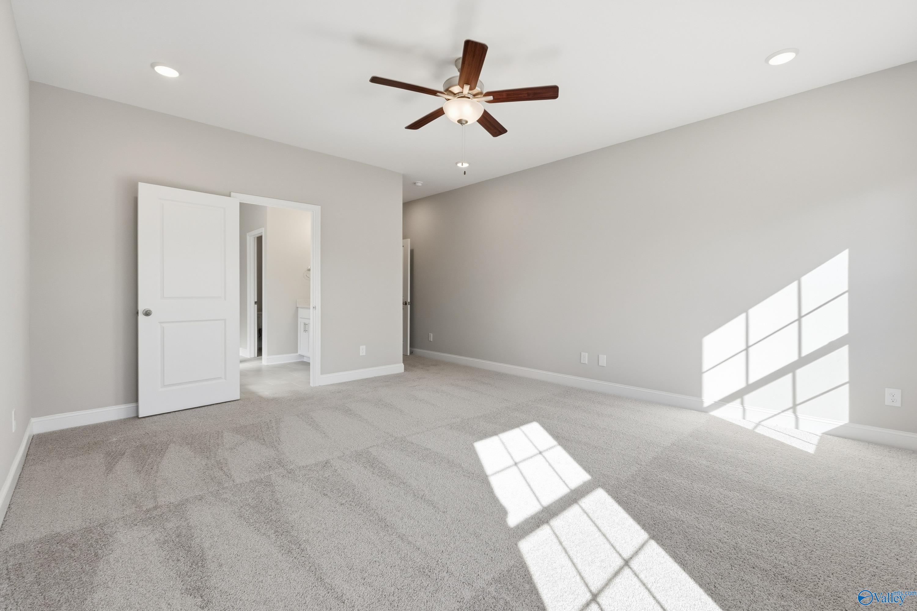 Spacious master bedroom with ceiling fan, gray carpet, and en-suite bath in Davidson Homes The Rockford, Creekside, Harvest, Alabama