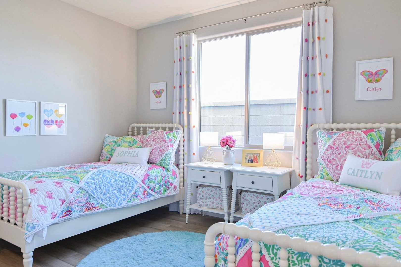 Cozy twin girls' bedroom in The Harmony home with colorful patchwork quilts, butterfly art, and white spindle beds