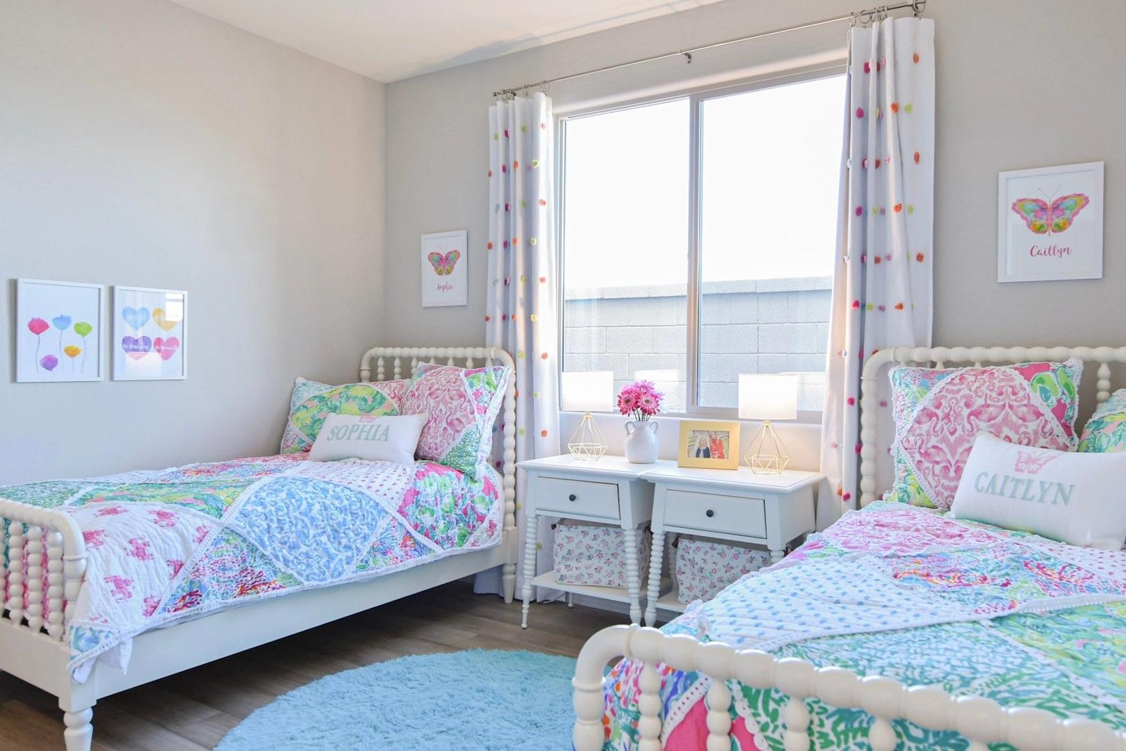 Cozy girls' shared bedroom in The Harmony B featuring twin beds with colorful quilts, butterfly decor, and large windows