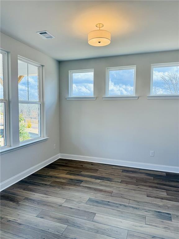 Bright empty room with light gray walls, warm hardwood floors, and triple windows with natural light in The Danbury C, Buford, Georgia