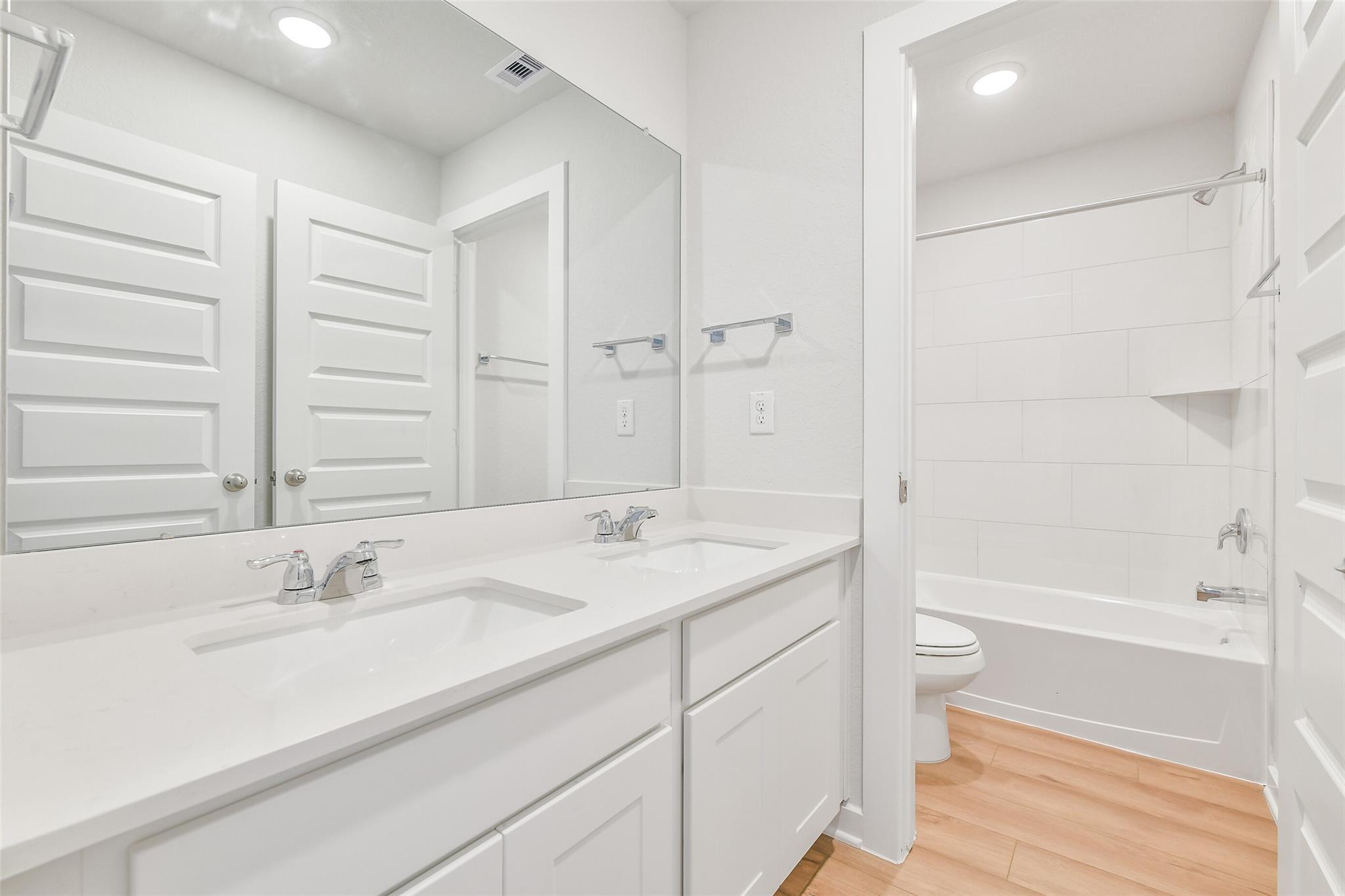 Bright bathroom featuring double vanity, white cabinetry, bathtub, and recessed lighting in The Blanco E 4-bedroom home, Magnolia, Texas