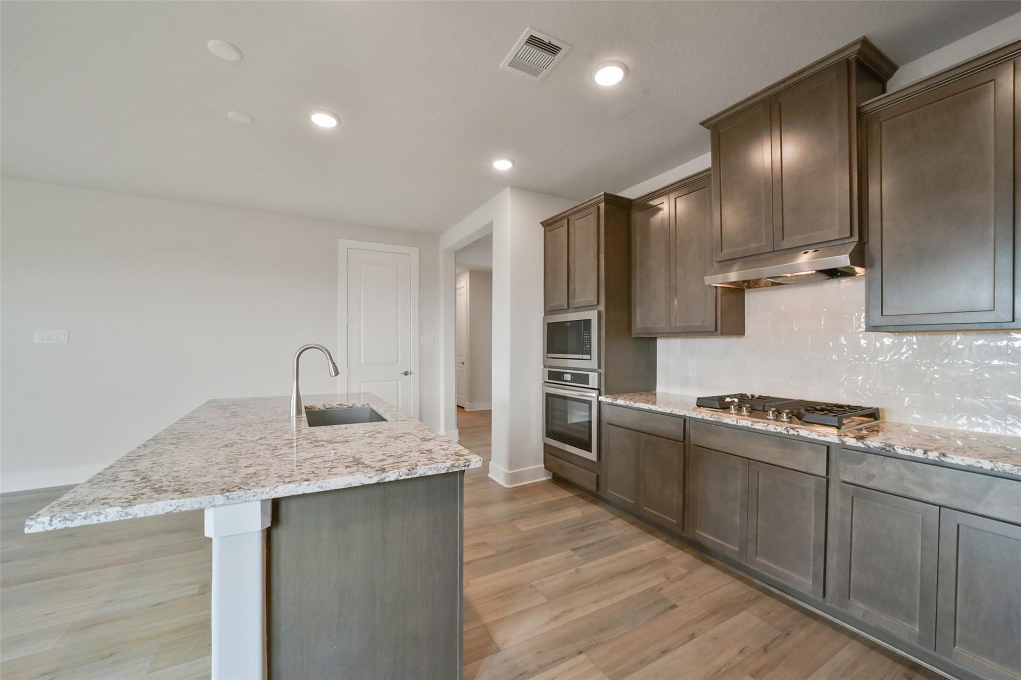 Modern kitchen with quartz island sink, stainless double ovens, gas range, and shaker cabinets in Davidson Homes The Zion A, Texas City