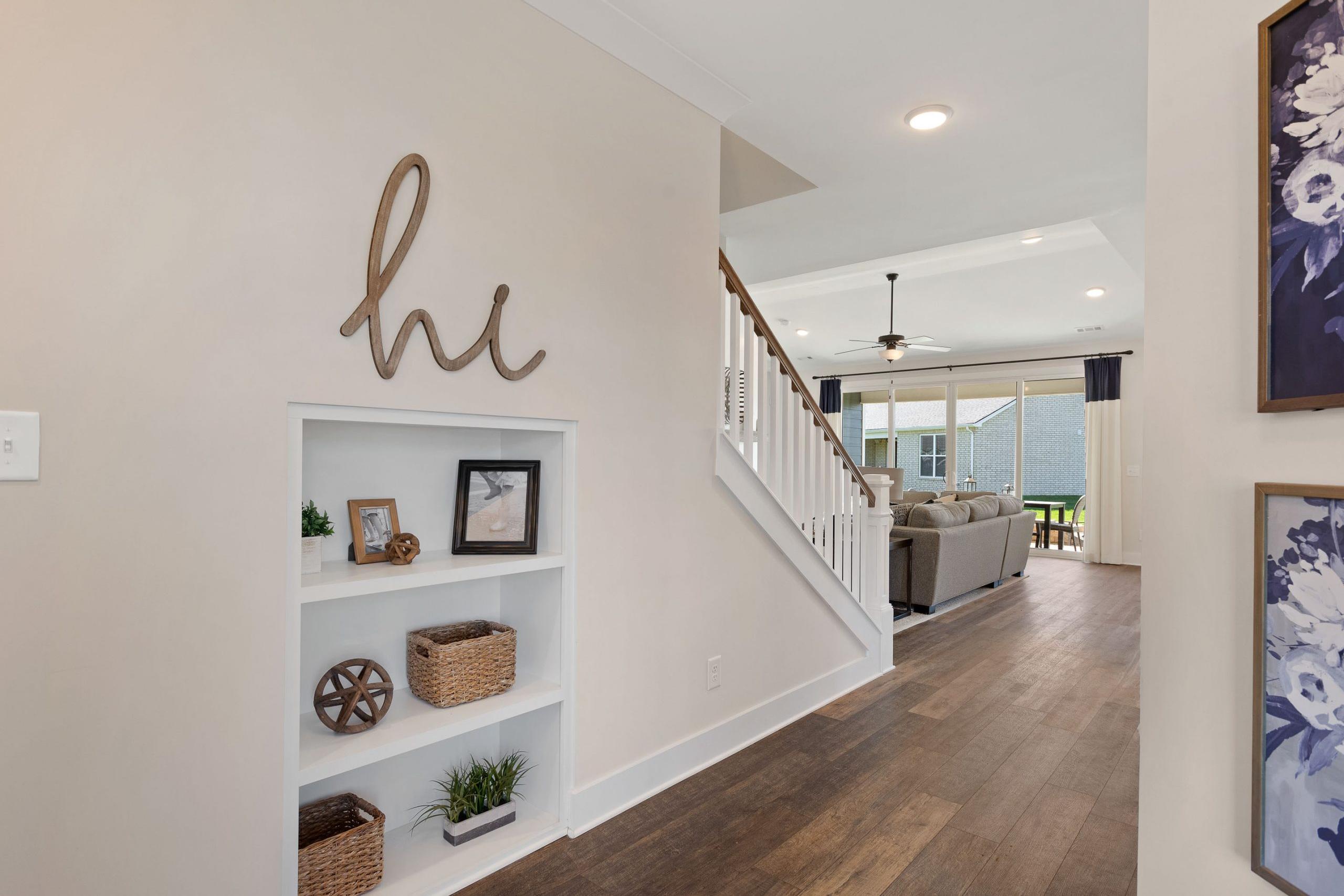 Welcoming entryway at Rivers Edge in Murfreesboro TN with wooden "hi" sign, built-in shelves, staircase, and open living room with hardwood floors