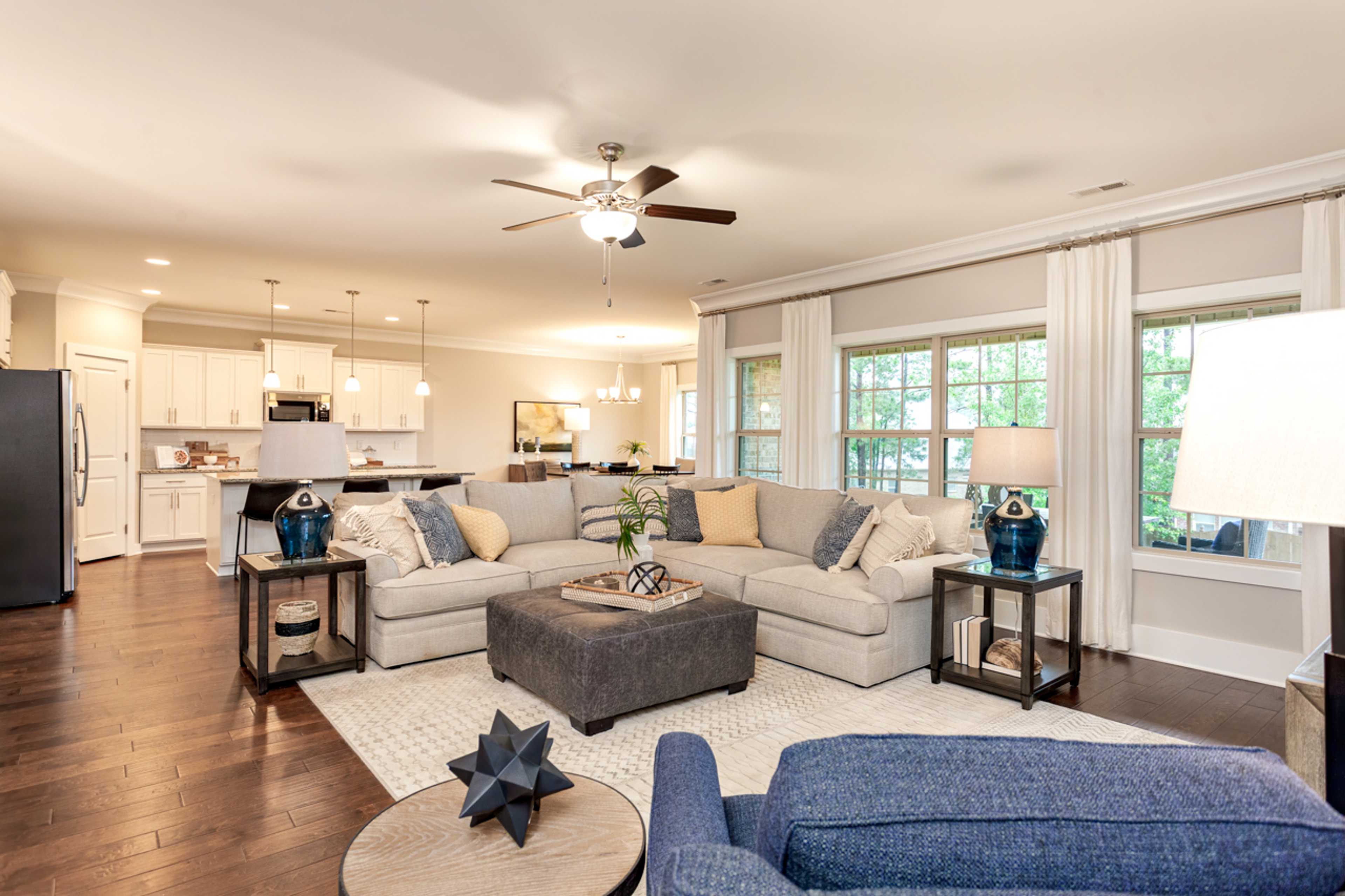 Open-concept living room and kitchen in Laurenwood Preserve, Madison AL with hardwood floors, beige L-shaped sofa, and large windows