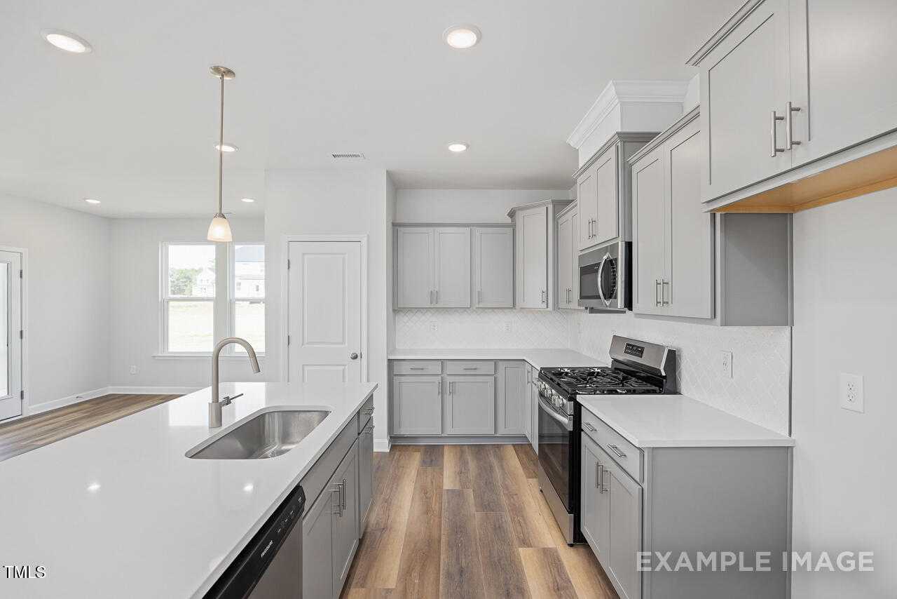 Modern kitchen with shaker cabinets, stainless appliances, quartz island in Davidson Homes The Daphne C, Lillington, NC