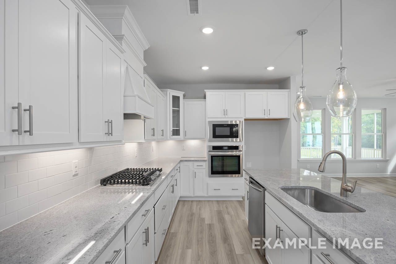 Modern gourmet kitchen at Retreat at North Main by Davidson Homes in Lillington, NC, with white cabinets and granite island.