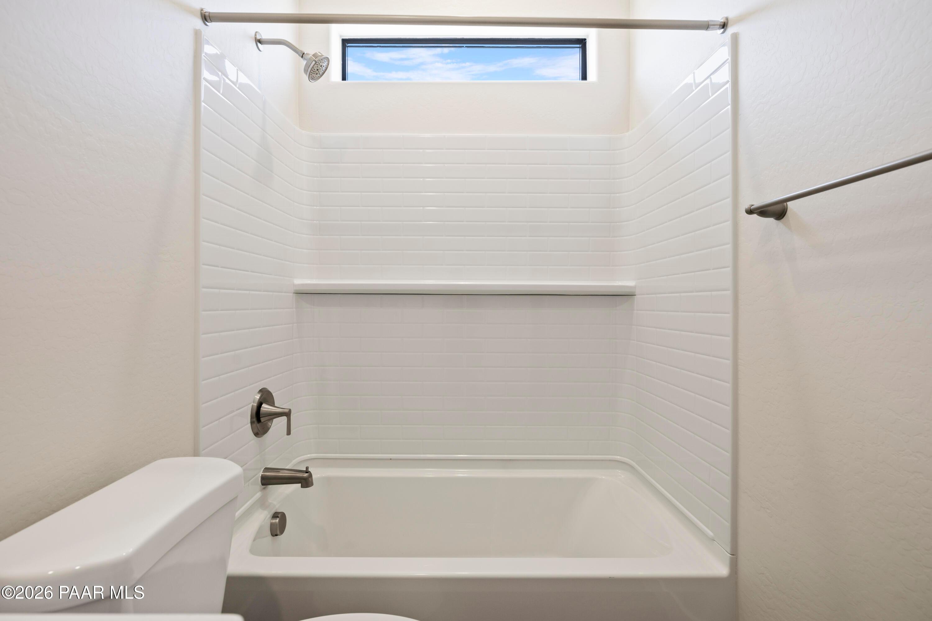 Modern white subway tile bathroom with glass shower enclosure, deep soaking tub, and clerestory window in The Soleil E home, Prescott, Arizona
