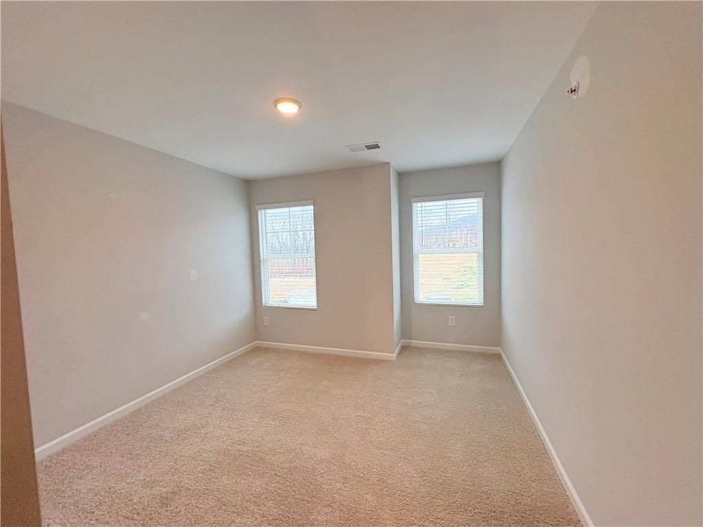 Empty bedroom with beige carpet, light gray walls, double windows, and recessed lighting in Davidson Homes The Wake E, Cumming, GA