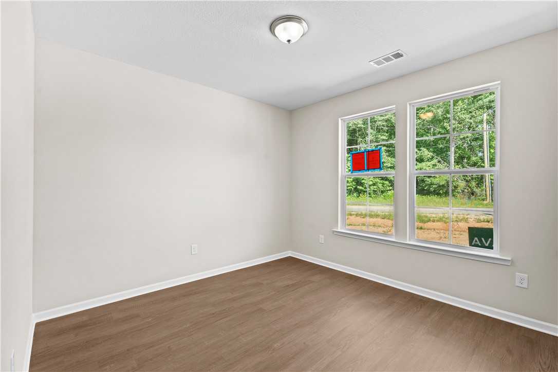Bright bedroom with neutral walls, hardwood floors, and large windows overlooking lush greenery in Evermore Homes The Orion, Cusseta Alabama