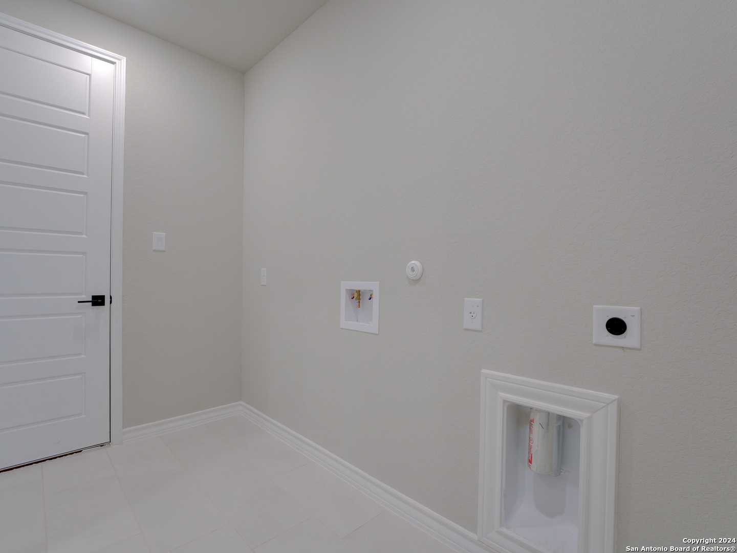 Modern laundry room featuring washer-dryer hookups, utility sink, and beige walls in The Summerlin A 4-bedroom home, Castroville, Texas