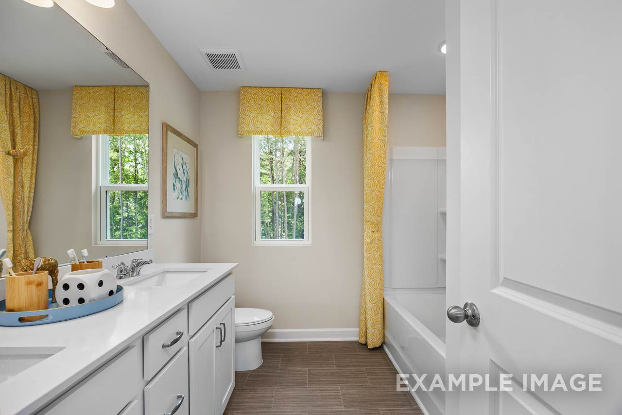 Bright bathroom in The Willow C-BF by Davidson Homes with white double vanity, tub, and yellow accents.