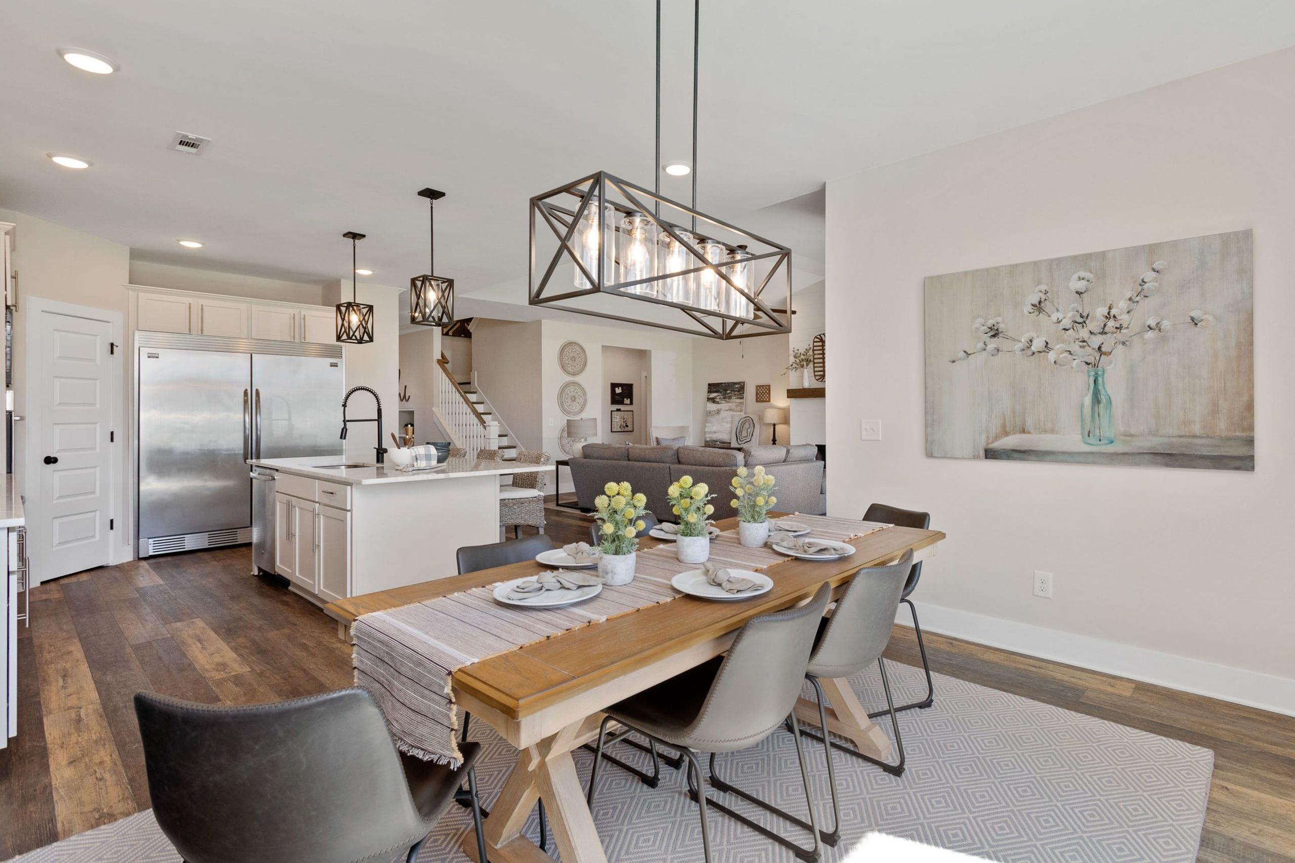 Open-concept kitchen dining area at Rivers Edge Murfreesboro TN with white cabinets hardwood floors pendant lights and farmhouse table
