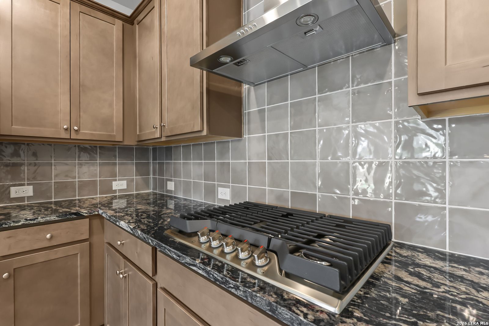 Gas cooktop with stainless vent hood, granite countertops and tile backsplash in Davidson Homes Daphne I kitchen, Bricewood San Antonio