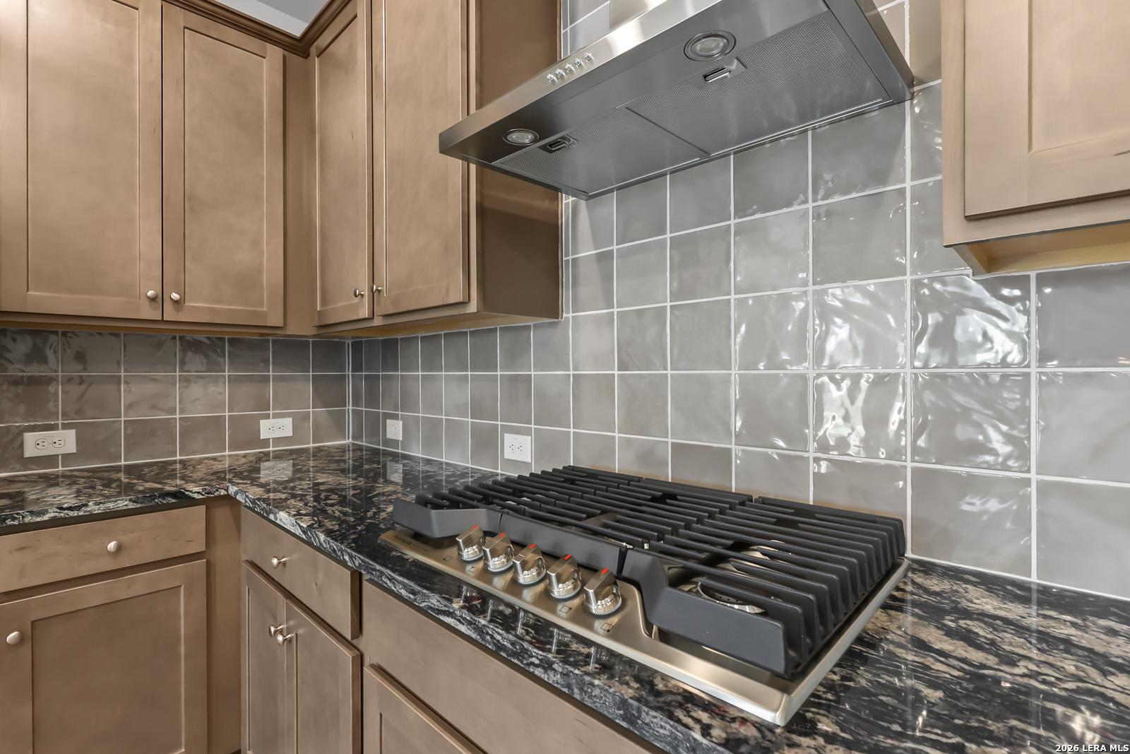 Gas cooktop with stainless vent hood, granite countertops and tile backsplash in Davidson Homes Daphne I kitchen, Bricewood San Antonio