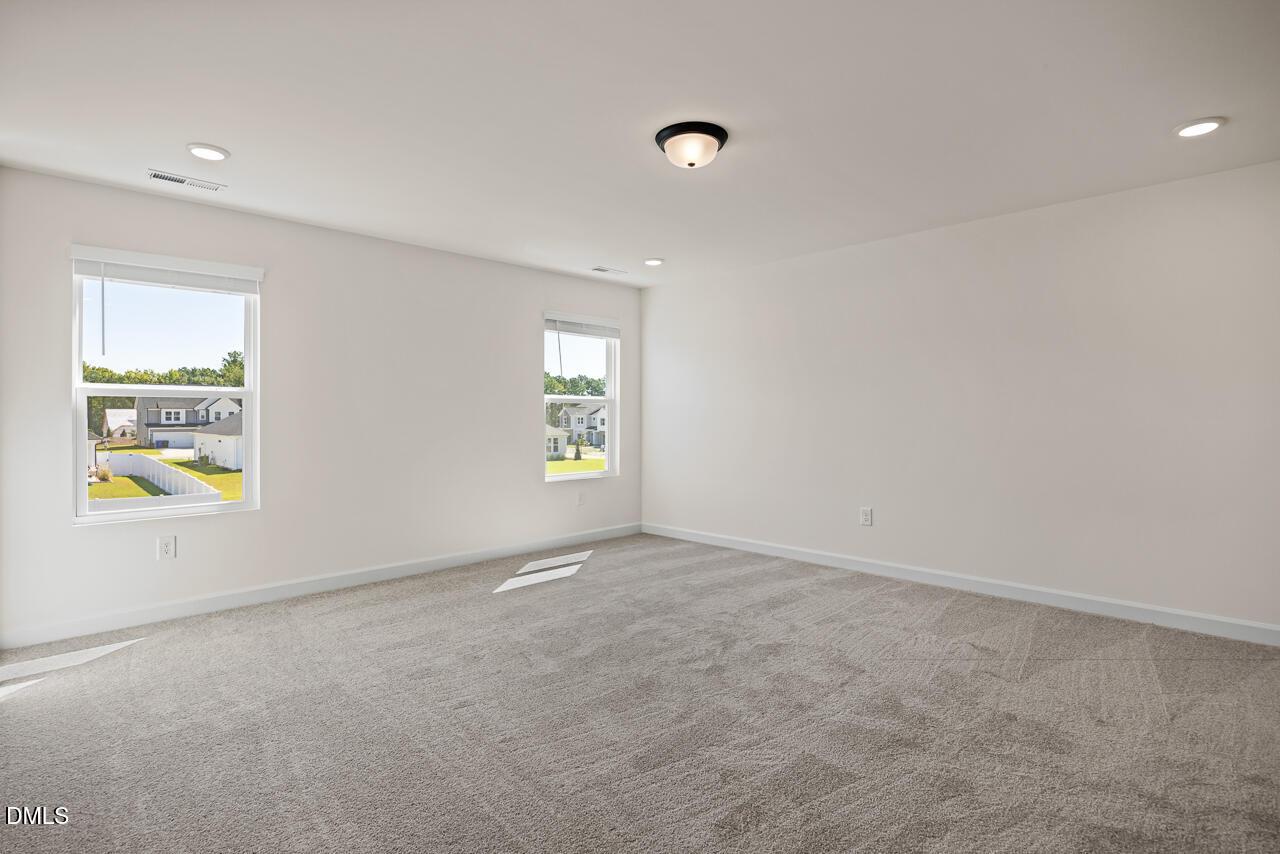Bright spacious bedroom with carpet flooring and windows overlooking neighborhood in Davidson Homes Hickory II B, Lillington NC