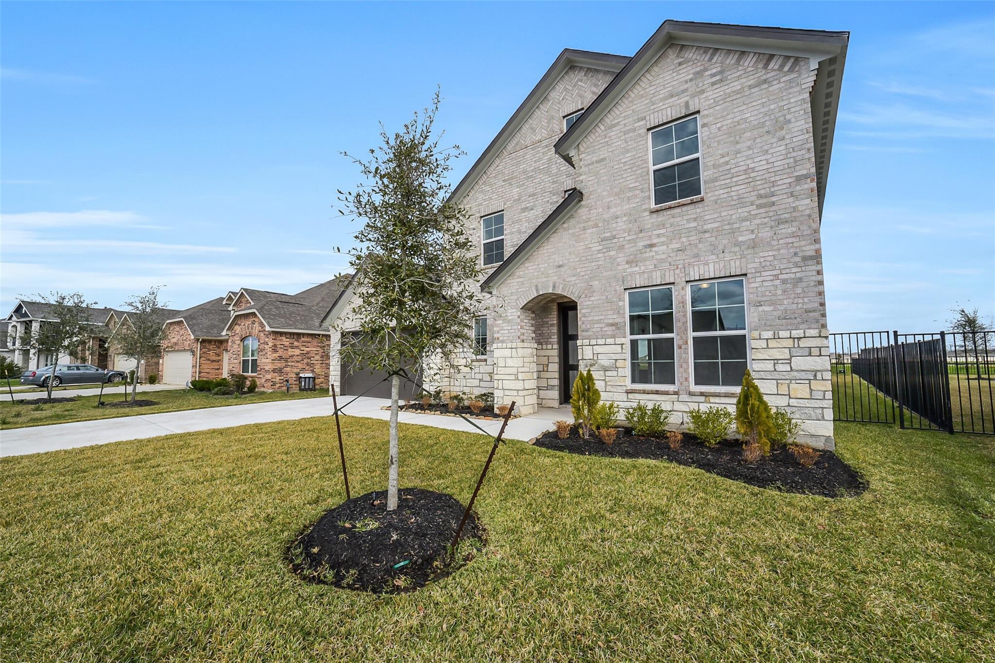 Modern two-story light brick home with 2-car garage, young oak tree, and landscaped front yard in Sierra Vista, Rosharon, Texas