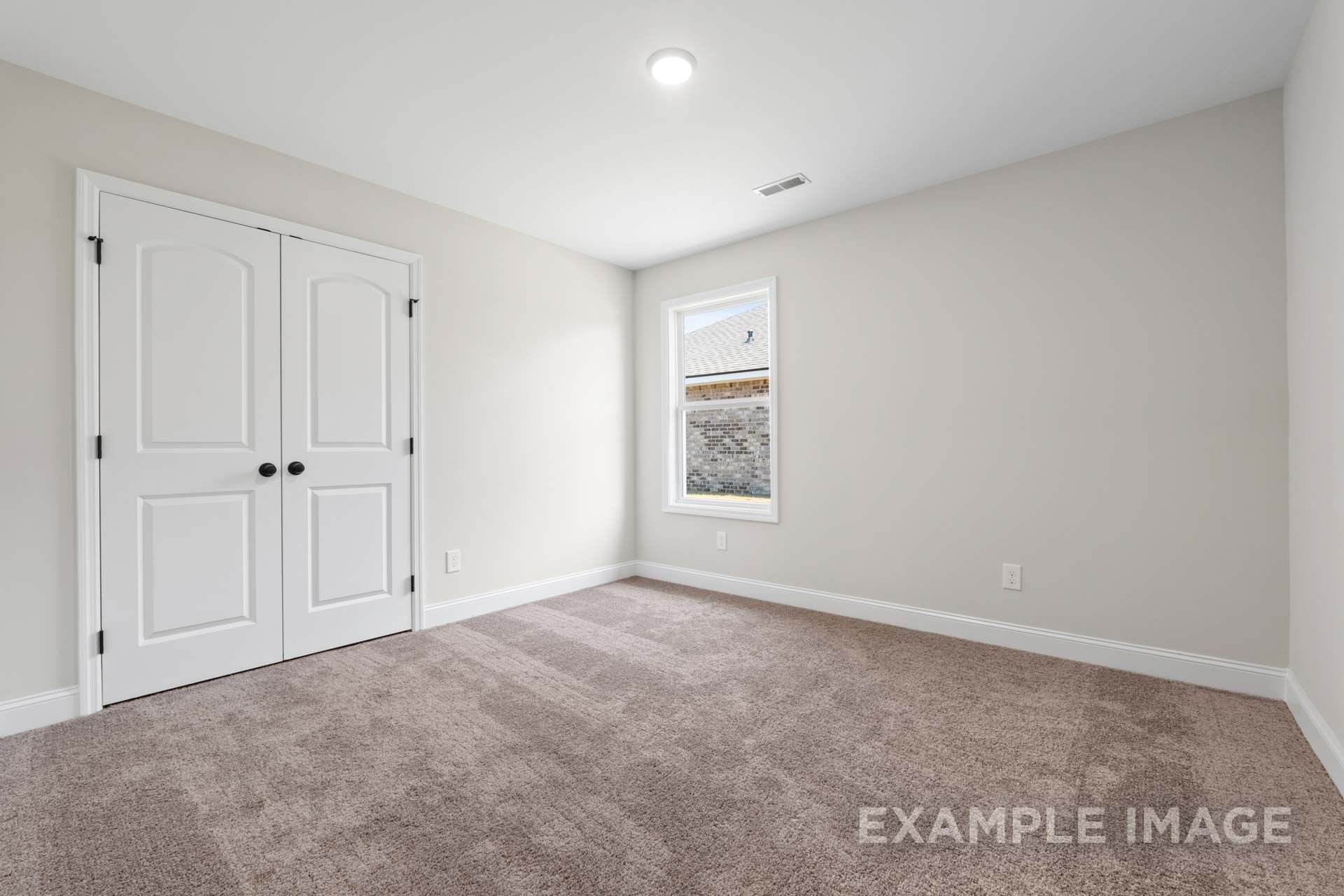 Spacious bedroom in The Holly M home design with light gray walls, beige carpet, double white doors, and window