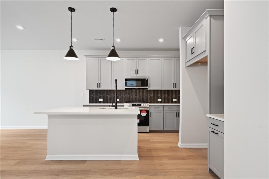 Modern white kitchen with large island, stainless appliances, subway tile backsplash, and hardwood floors in Davidson Homes Marion A, Kennesaw GA