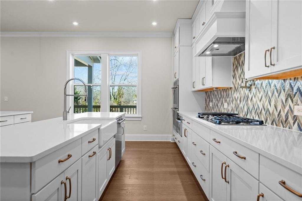 Modern white shaker kitchen with quartz island, stainless appliances, metallic tile backsplash, and backyard view in Davidson Homes The Arlington A, East Cobb