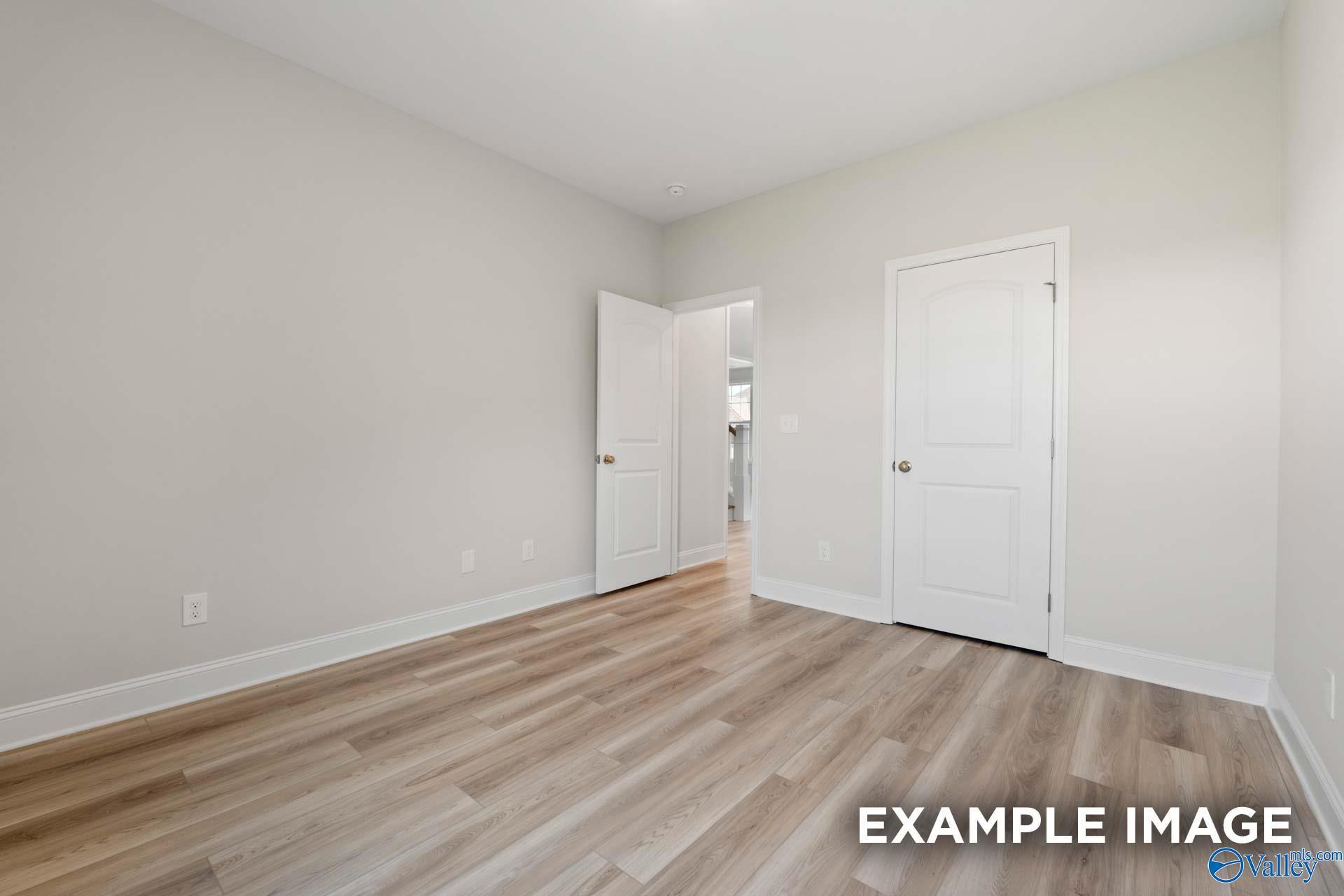 Spacious empty bedroom with light gray walls, laminate wood floors, and double doors in Davidson Homes Madison A, Toney, AL