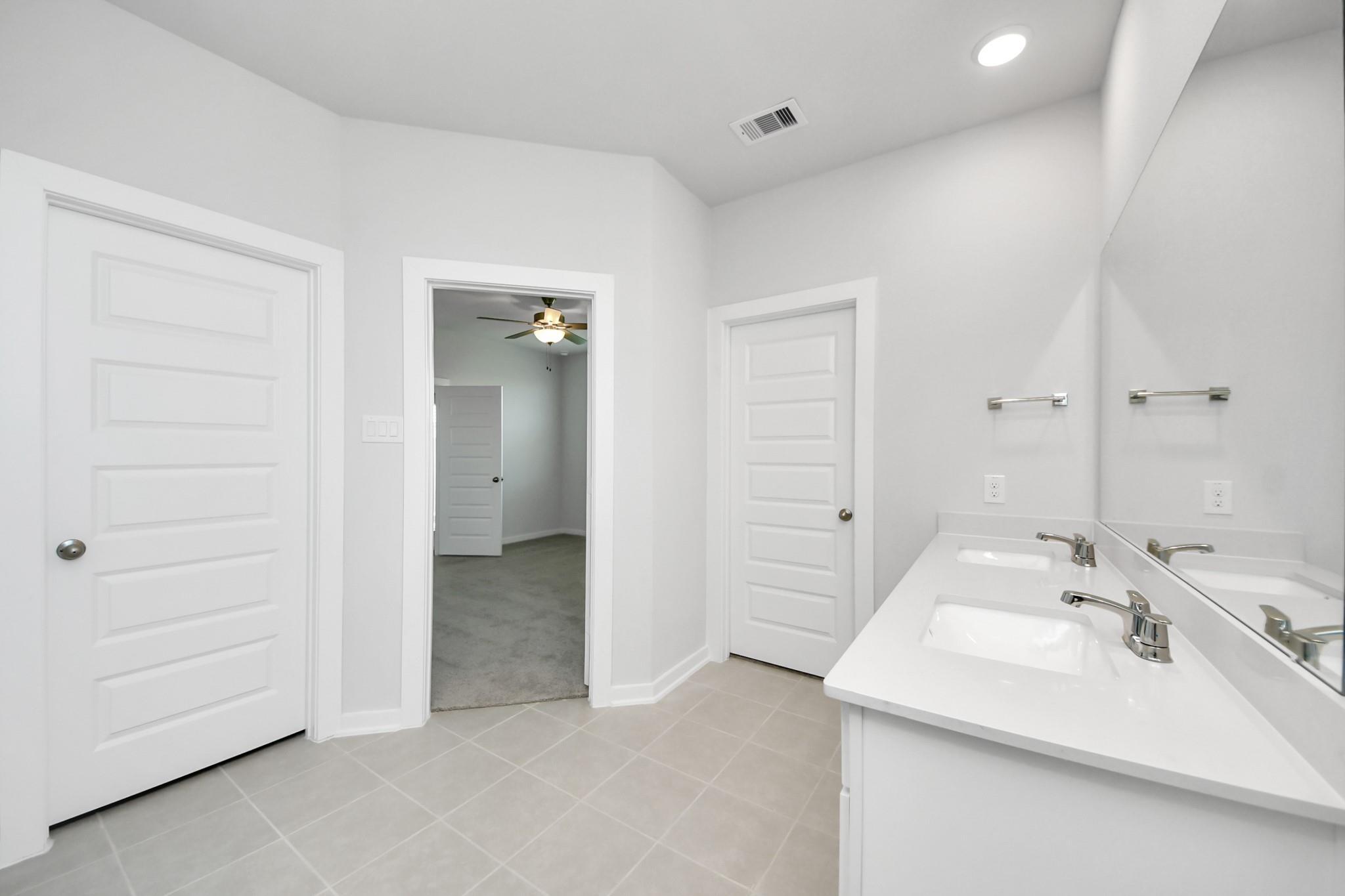 Bright white primary bathroom with dual-sink vanity and tile floor in The Costa A floor plan by Davidson Homes, Emberly, Beasley, TX