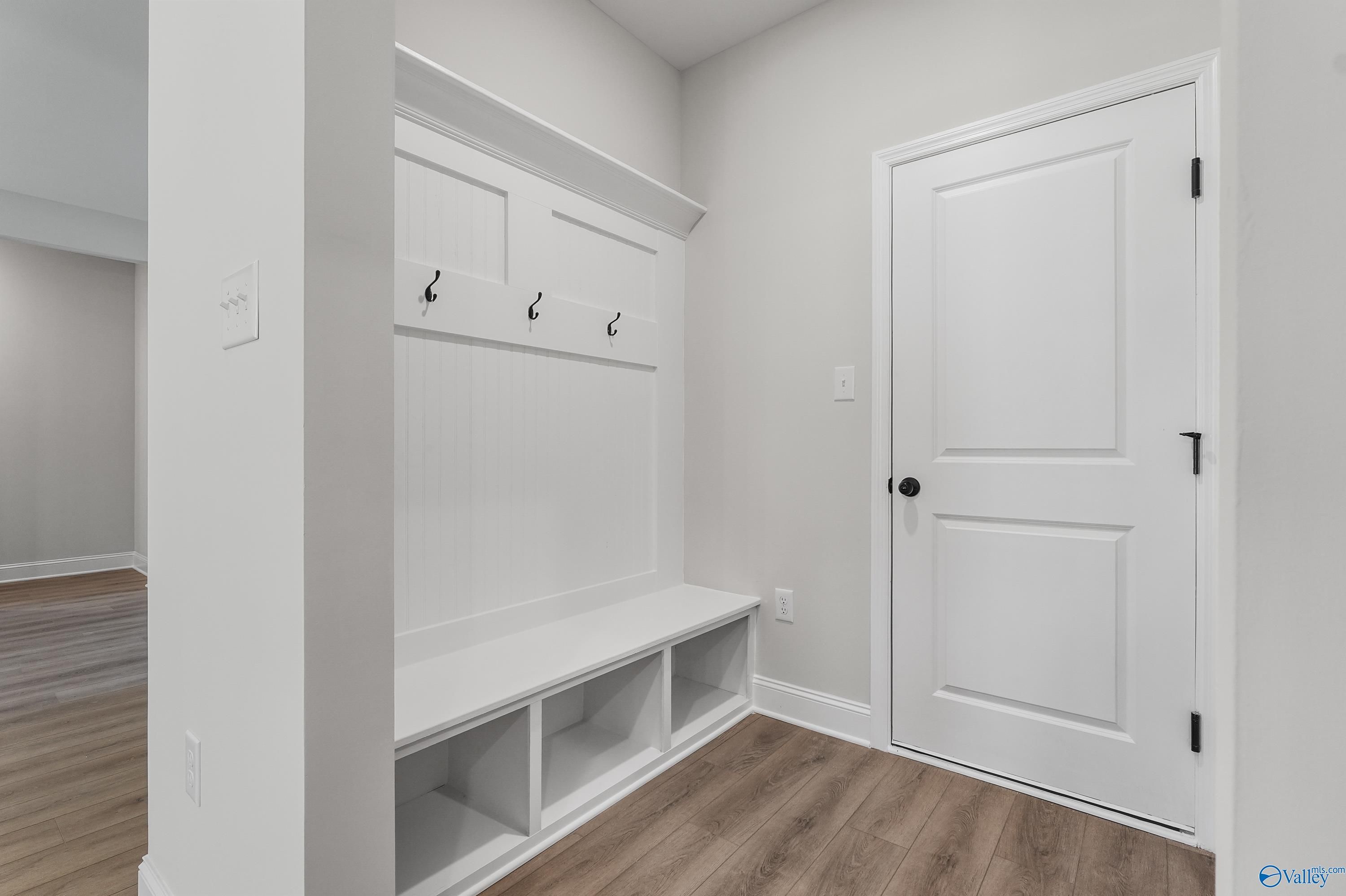 Spacious mudroom with white built-in cabinetry, coat hooks, bench, and door in Davidson Homes The Montgomery C, Decatur, AL