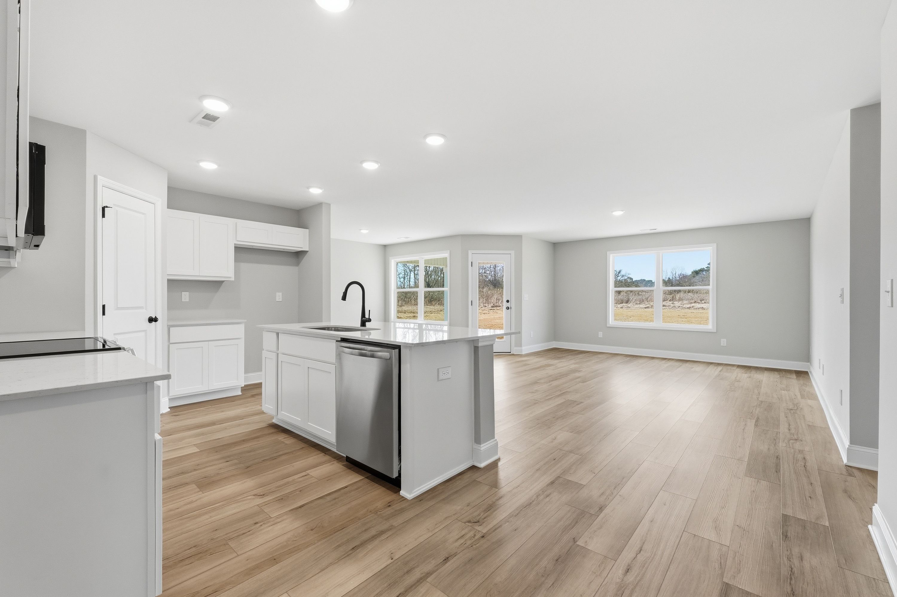 Spacious open-concept kitchen in The Daphne V with white shaker cabinets, quartz island, hardwood floors, and large windows