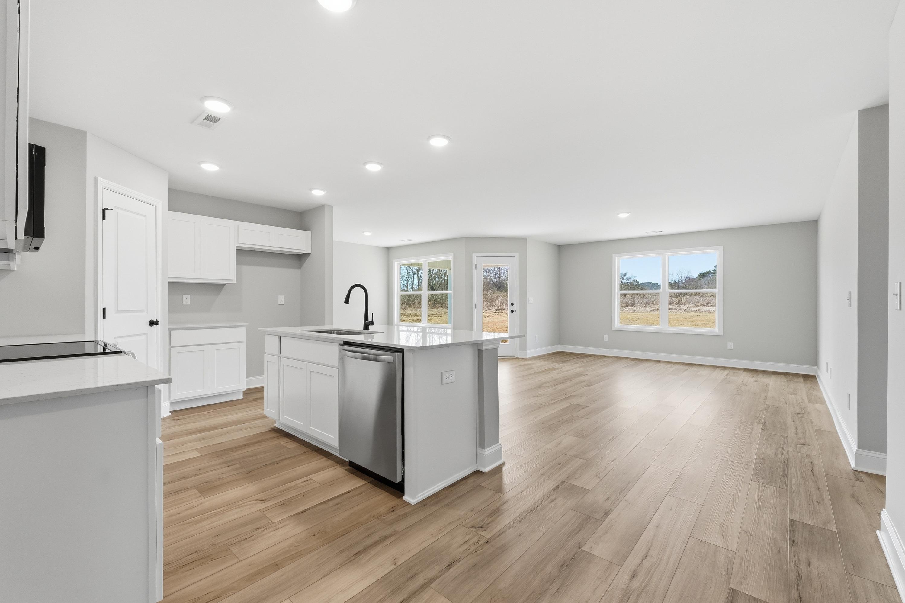 Spacious open-concept kitchen in The Daphne V with white shaker cabinets, quartz island, hardwood floors, and large windows