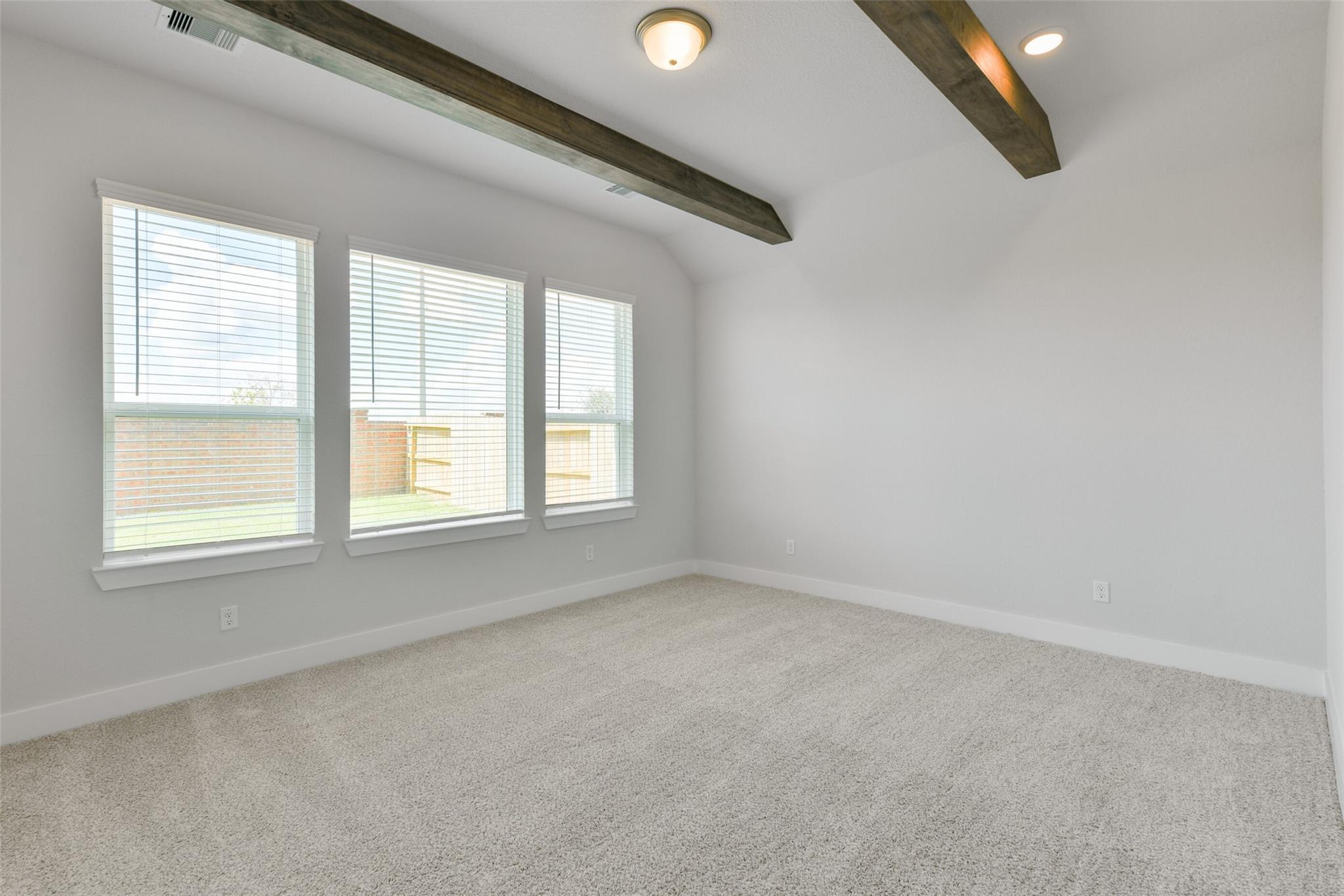Spacious bedroom with wooden beam ceiling, three large windows with blinds, and plush carpet in Davidson Homes The Edward A, Lago Mar, Texas