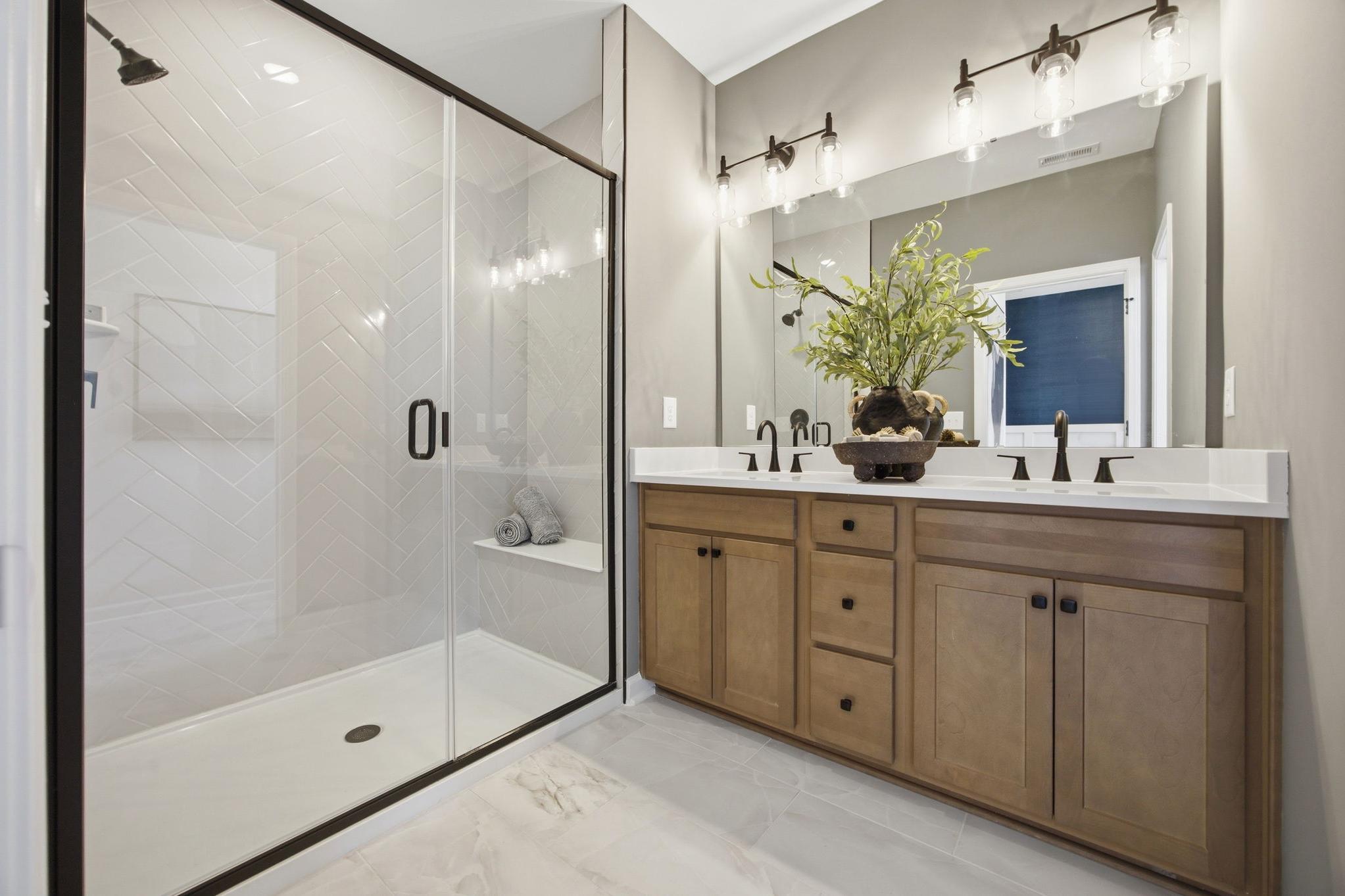 Modern master bathroom at Forestville Yard in Knightdale NC with glass shower, herringbone tile, and wood double vanity