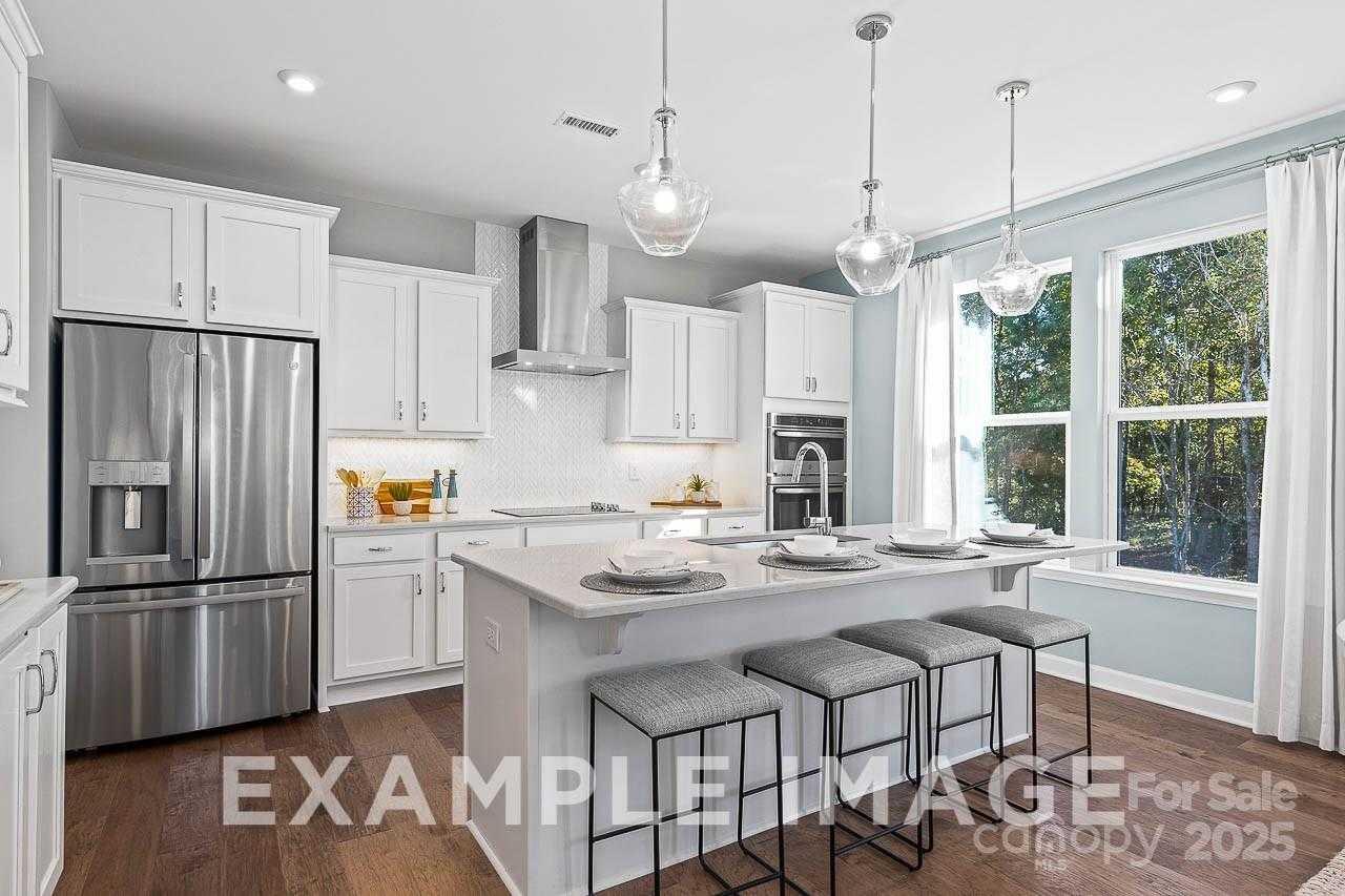 Modern white kitchen with stainless appliances, quartz island, pendant lights, and tree-view windows in Hemlock A by Davidson Homes, Belmont, NC