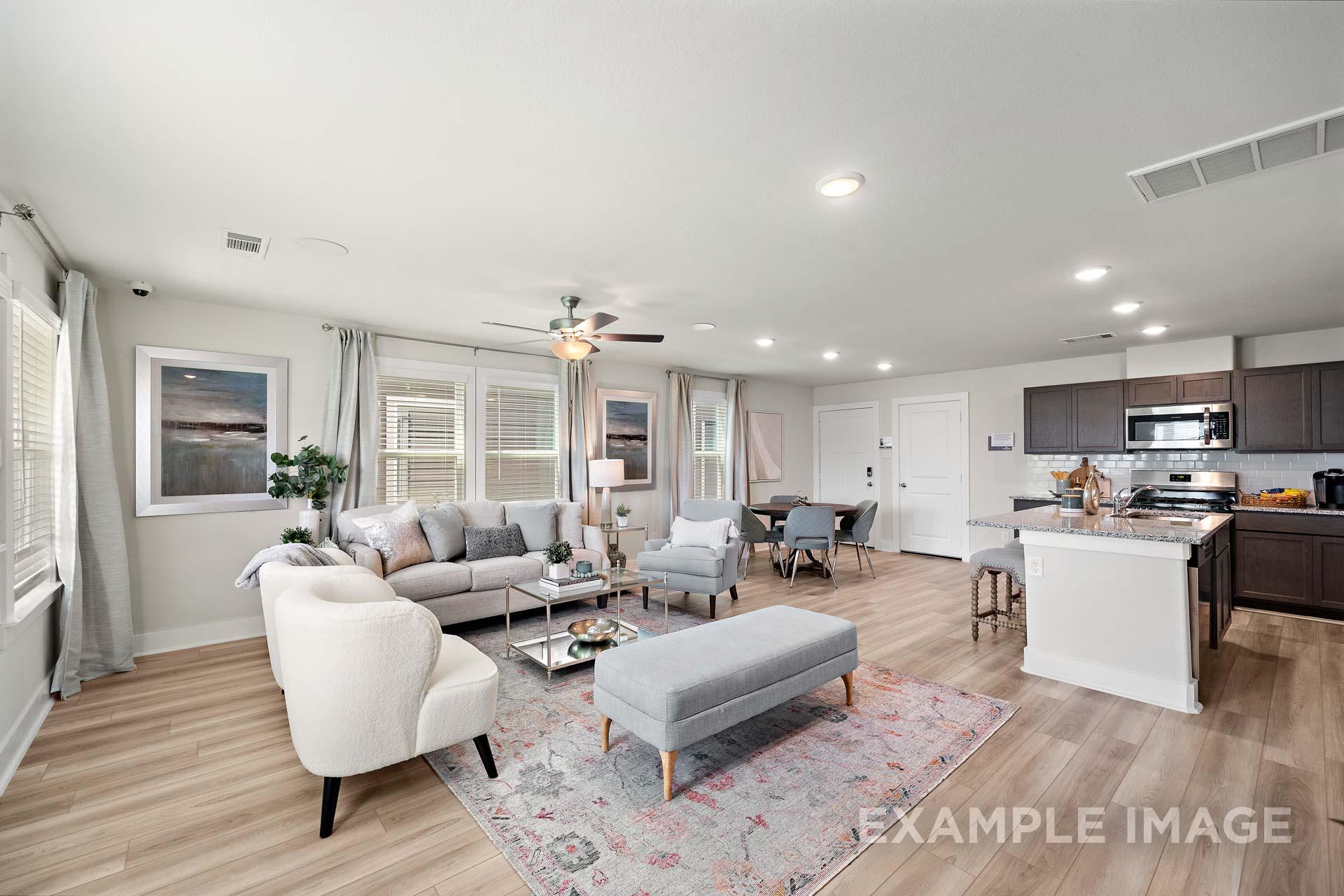 Spacious open-concept living room and kitchen in The Lily A home with gray sofa, white island, dining area, and hardwood floors