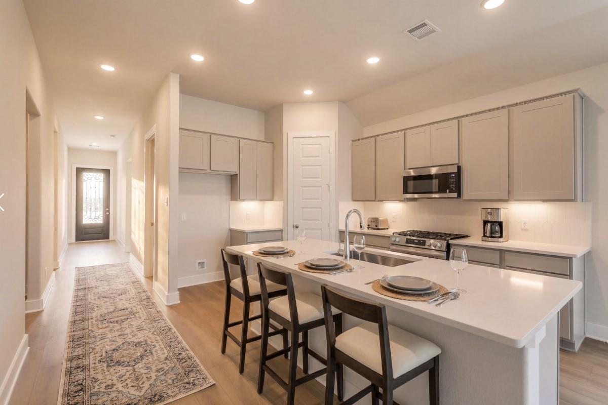 Modern open kitchen with white shaker cabinets, quartz island bar stools, and stainless appliances in Davidson Homes The Luna J, Katy, Texas