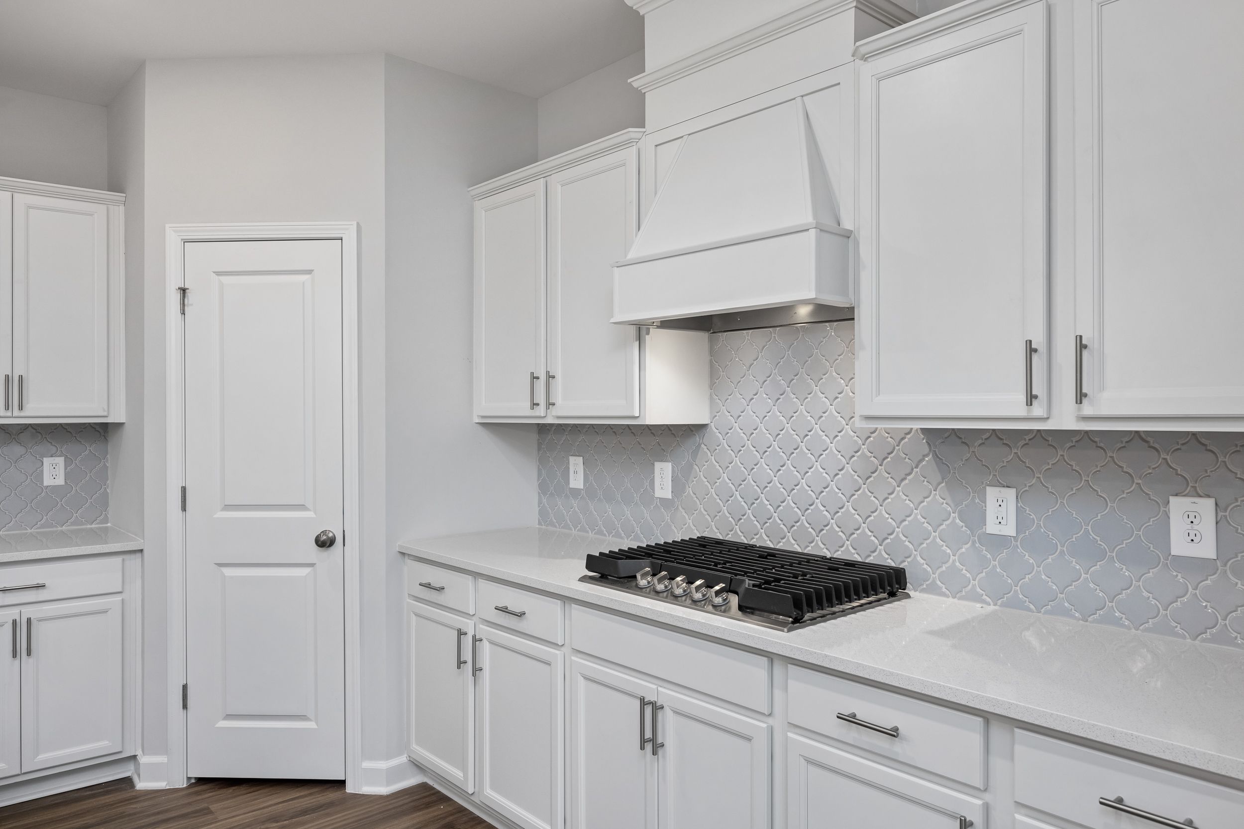 Modern kitchen in The Durham home featuring white shaker cabinets, quartz countertops, and a decorative tile backsplash.