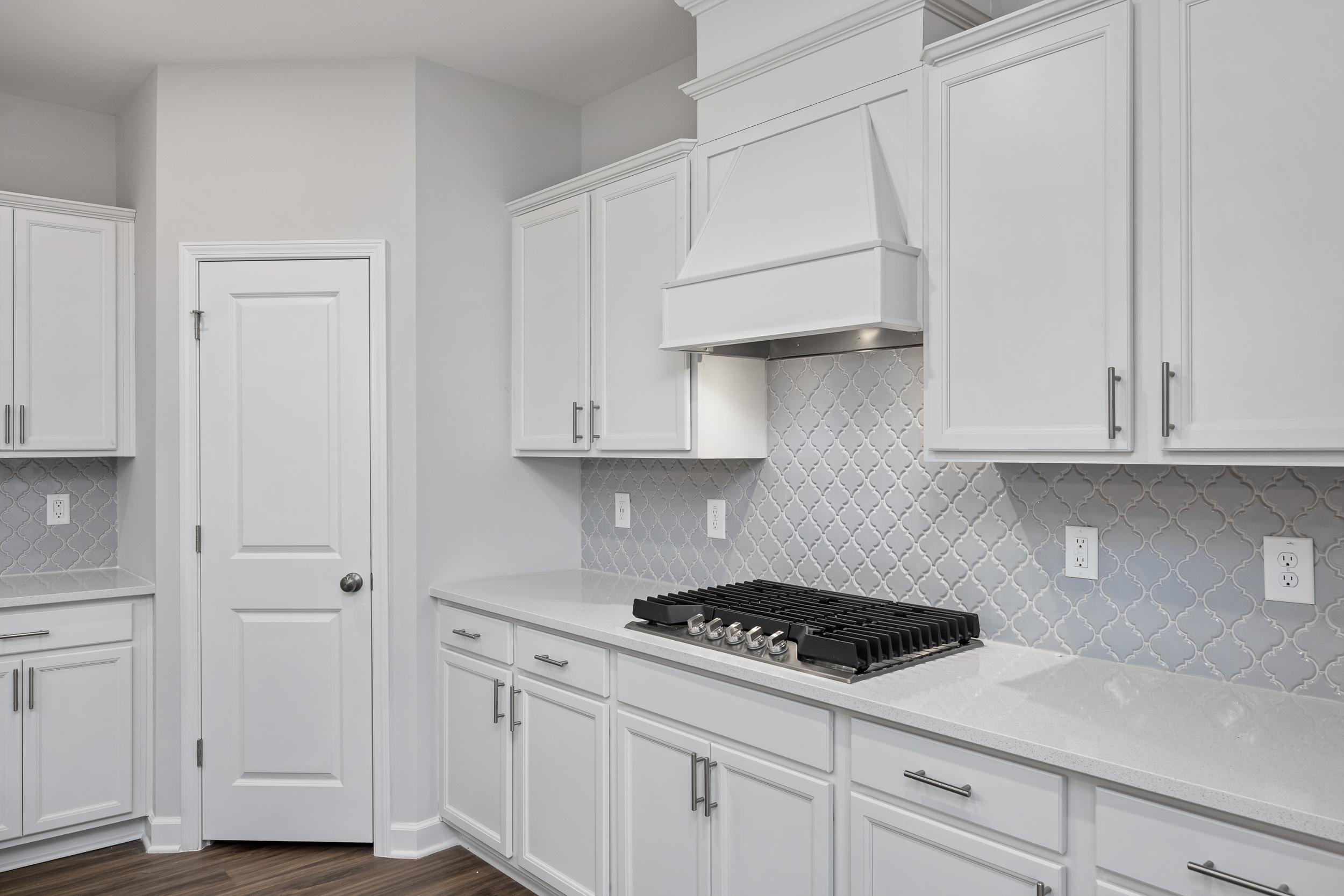 Modern kitchen in The Durham home featuring white shaker cabinets, quartz countertops, and a decorative tile backsplash.