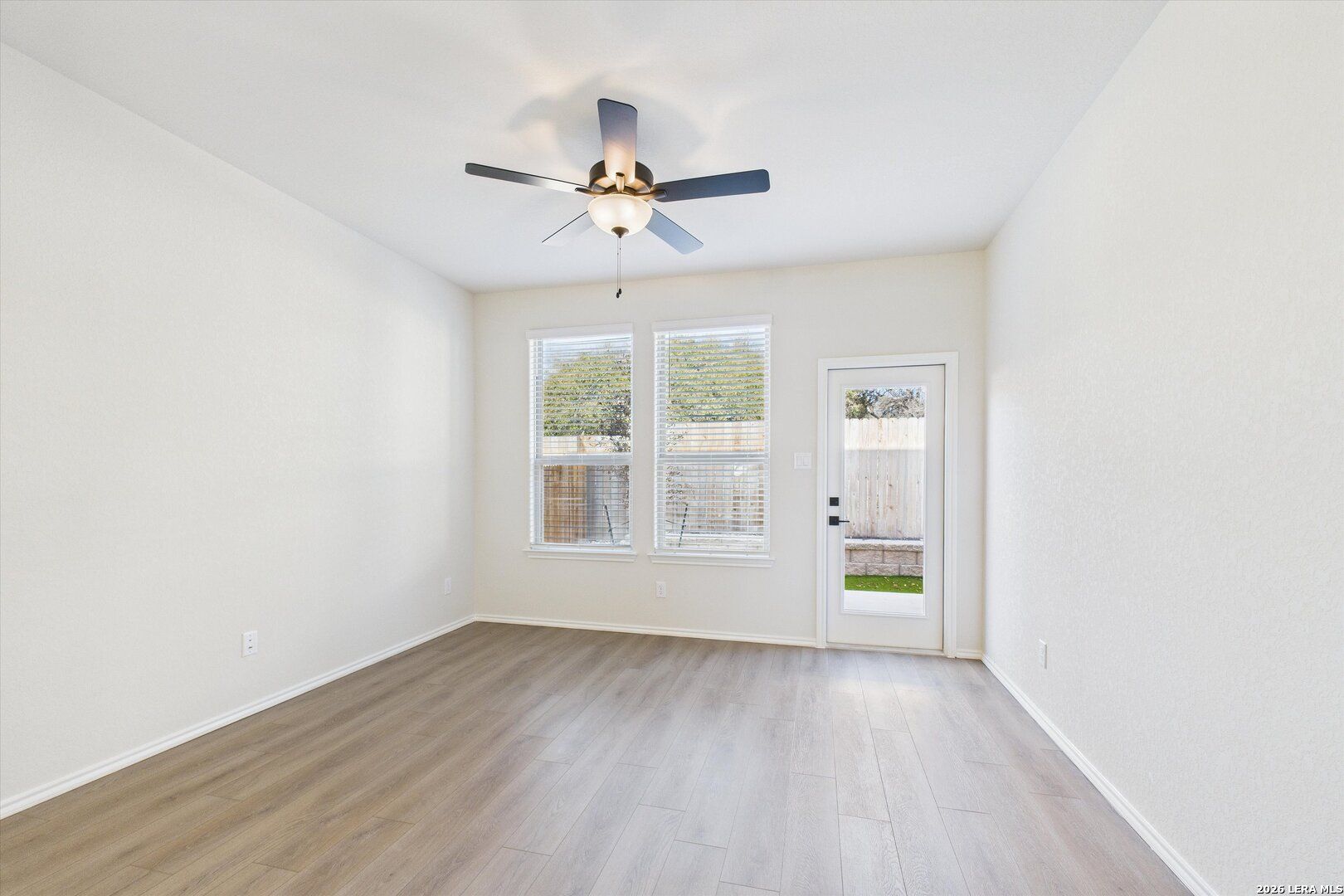 Bright family room with ceiling fan, large windows, and glass door to fenced backyard in Davidson Homes The Gillian B, San Antonio