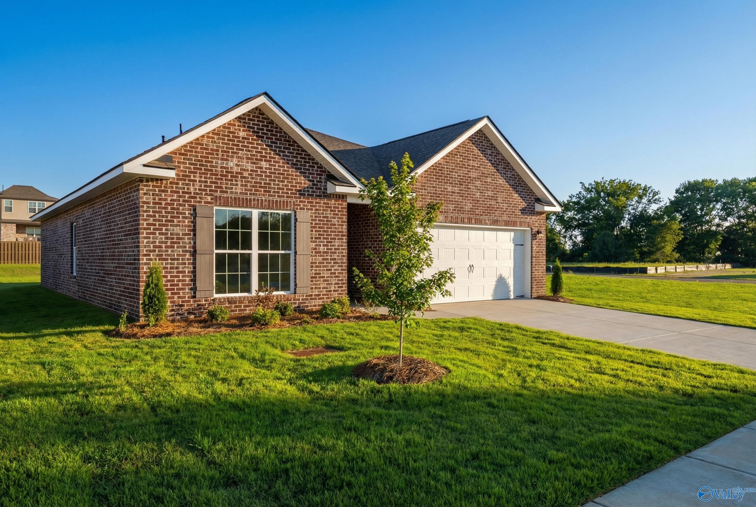 Brick 1-story home with 2-car garage, shuttered windows, young tree, and lush green lawn in Lynn Meadows, Meridianville, Alabama