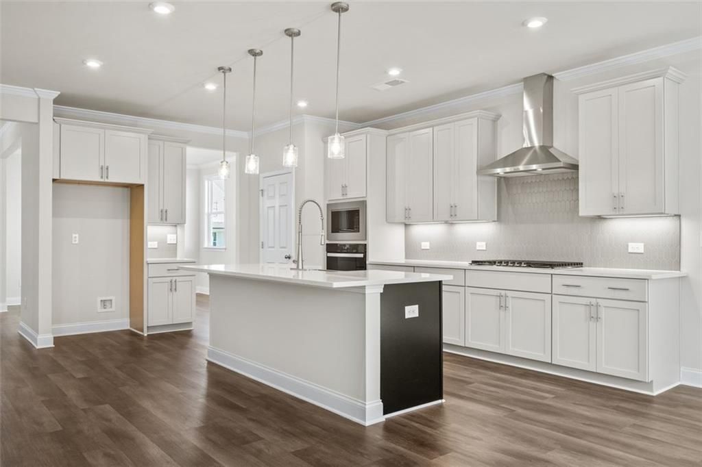 Modern white shaker kitchen with large island, stainless steel appliances, and hardwood floors in Davidson Homes The Ash C at Wehunt Meadows, Hoschton