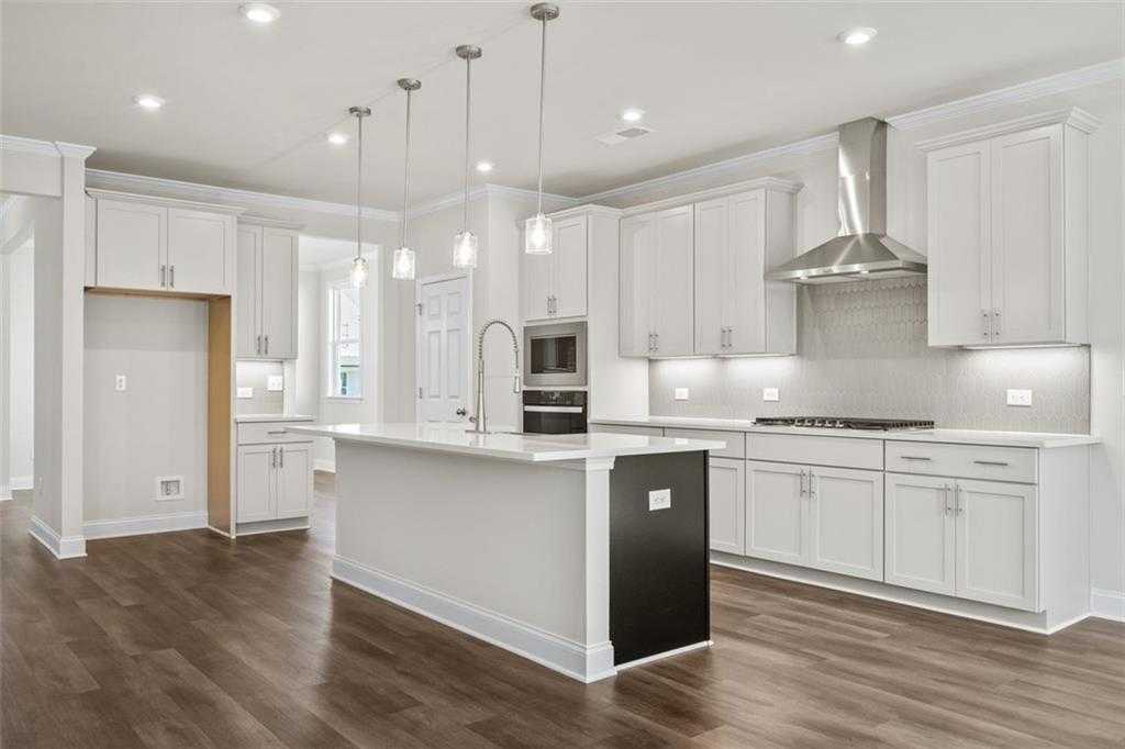 Modern white shaker kitchen with large island, stainless steel appliances, and hardwood floors in Davidson Homes The Ash C at Wehunt Meadows, Hoschton