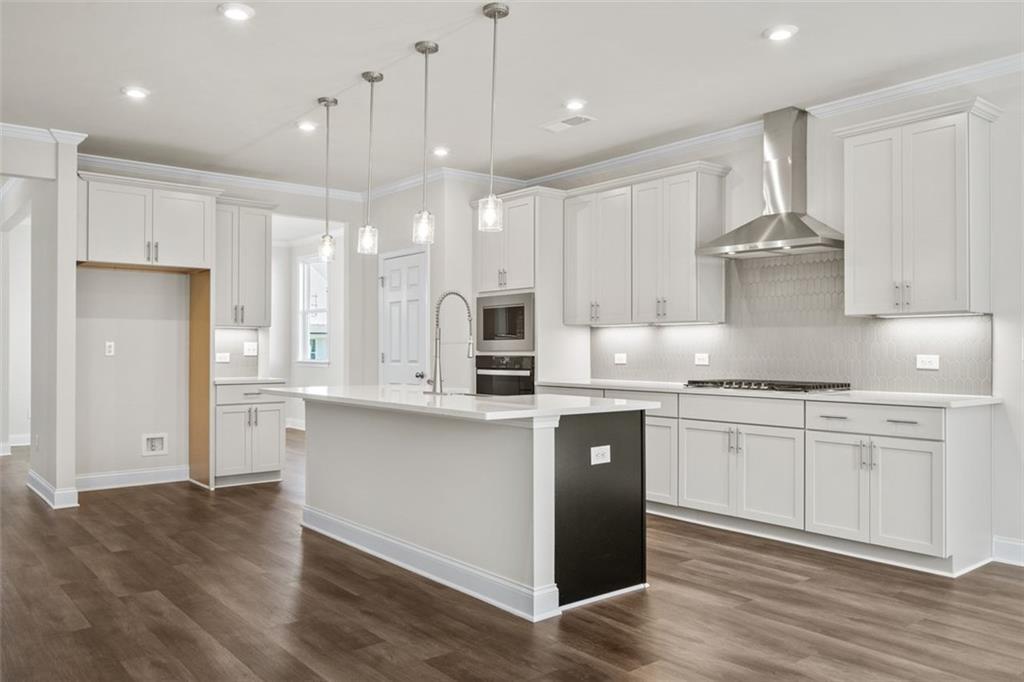 Modern white shaker kitchen with large island, stainless steel appliances, and hardwood floors in Davidson Homes The Ash C at Wehunt Meadows, Hoschton